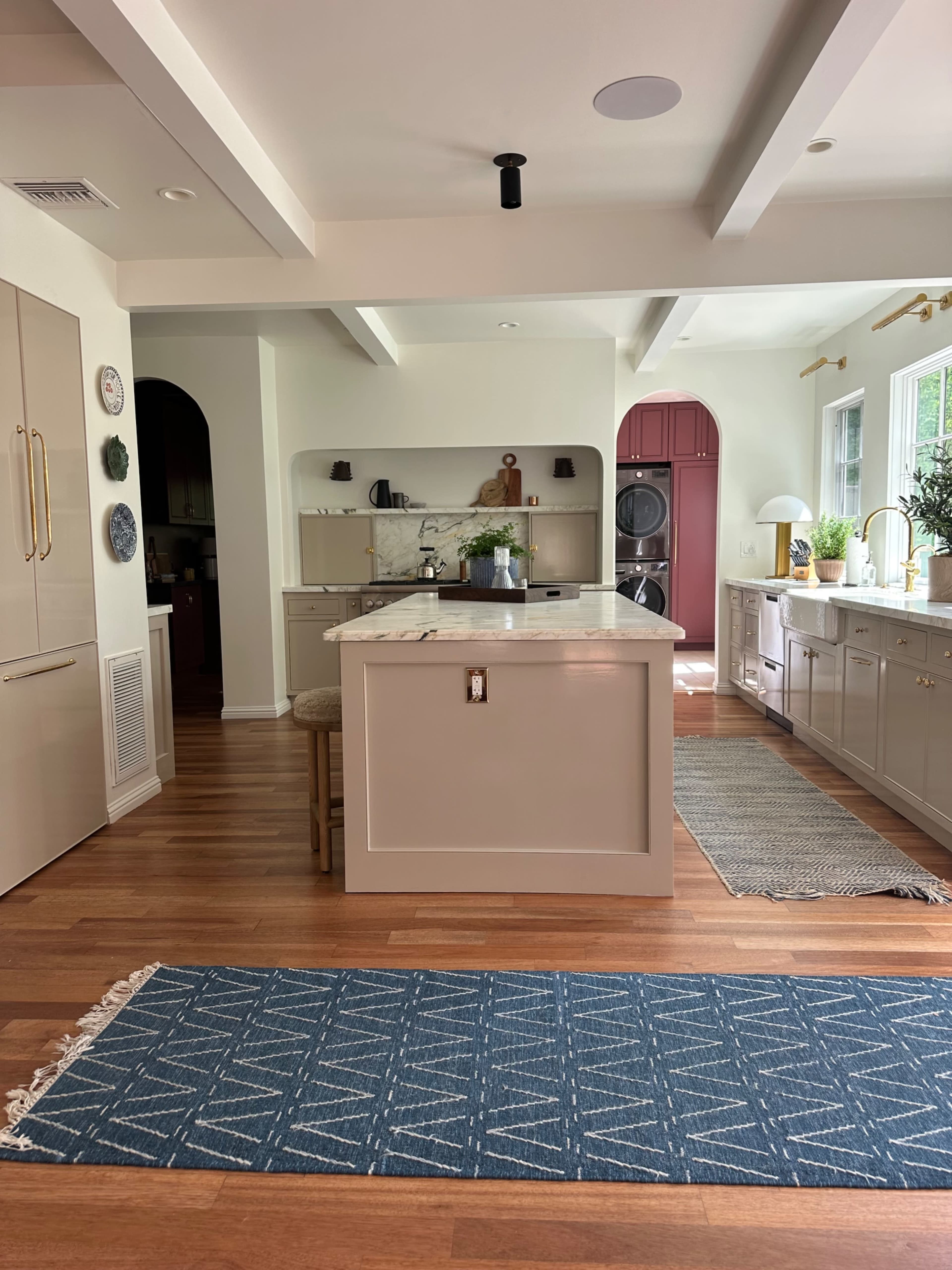 The image shows a spacious kitchen with an island, wooden floors, and a combination of cabinetry and natural light from large windows.
