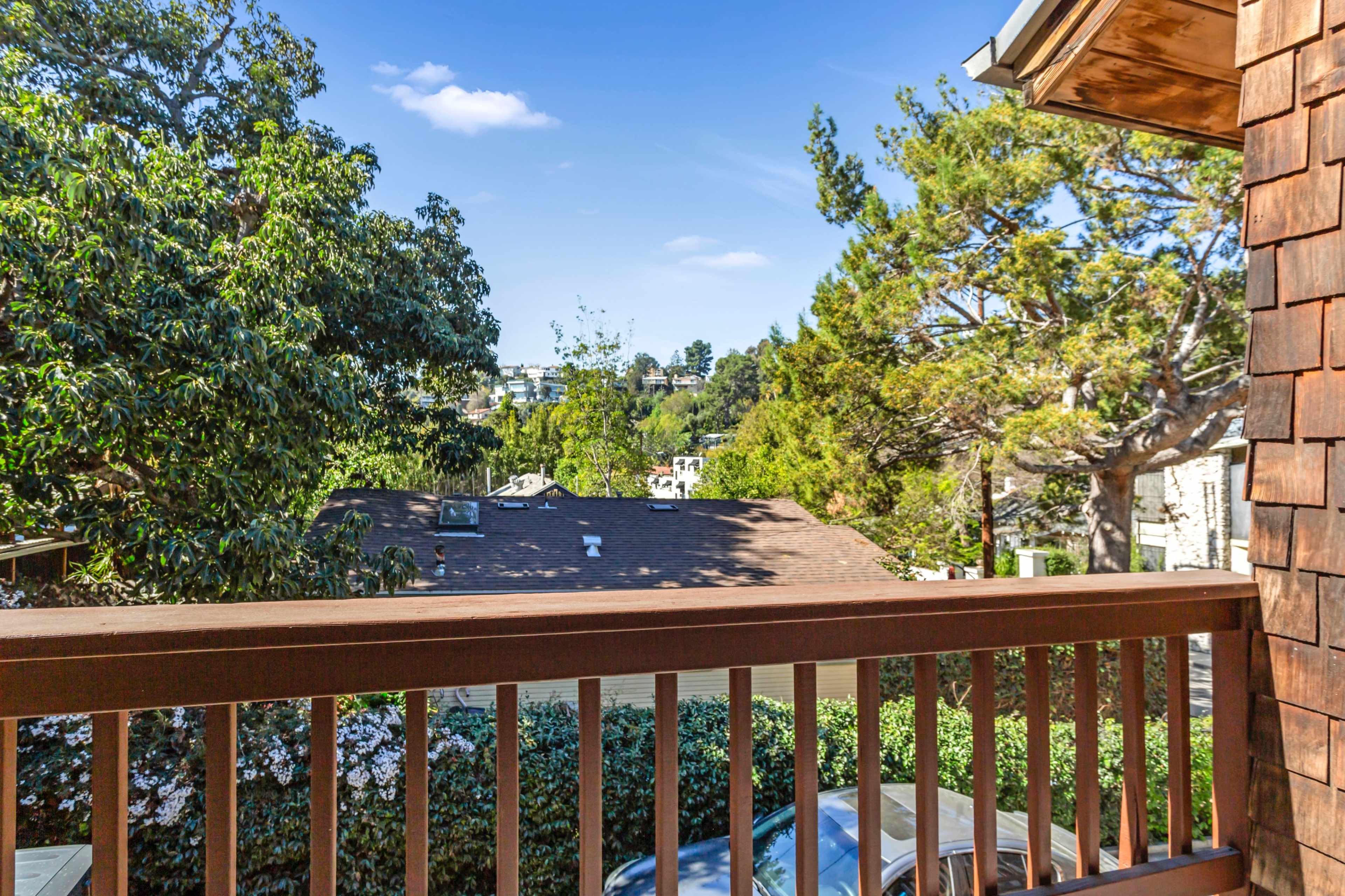 The image shows a balcony railing overlooking a landscape with trees and houses under a clear blue sky.