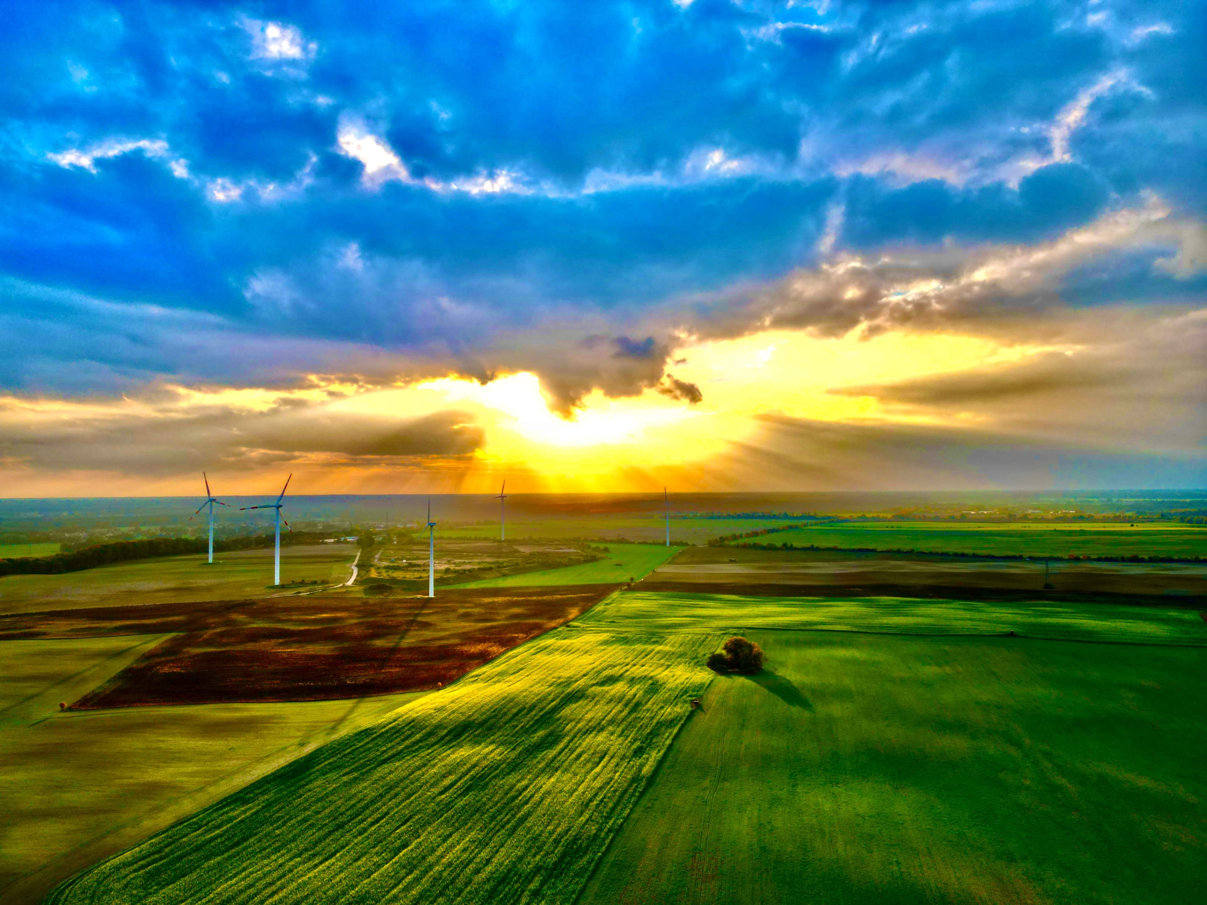 A vibrant sunset illuminates a landscape with wind turbines scattered across green and brown fields.