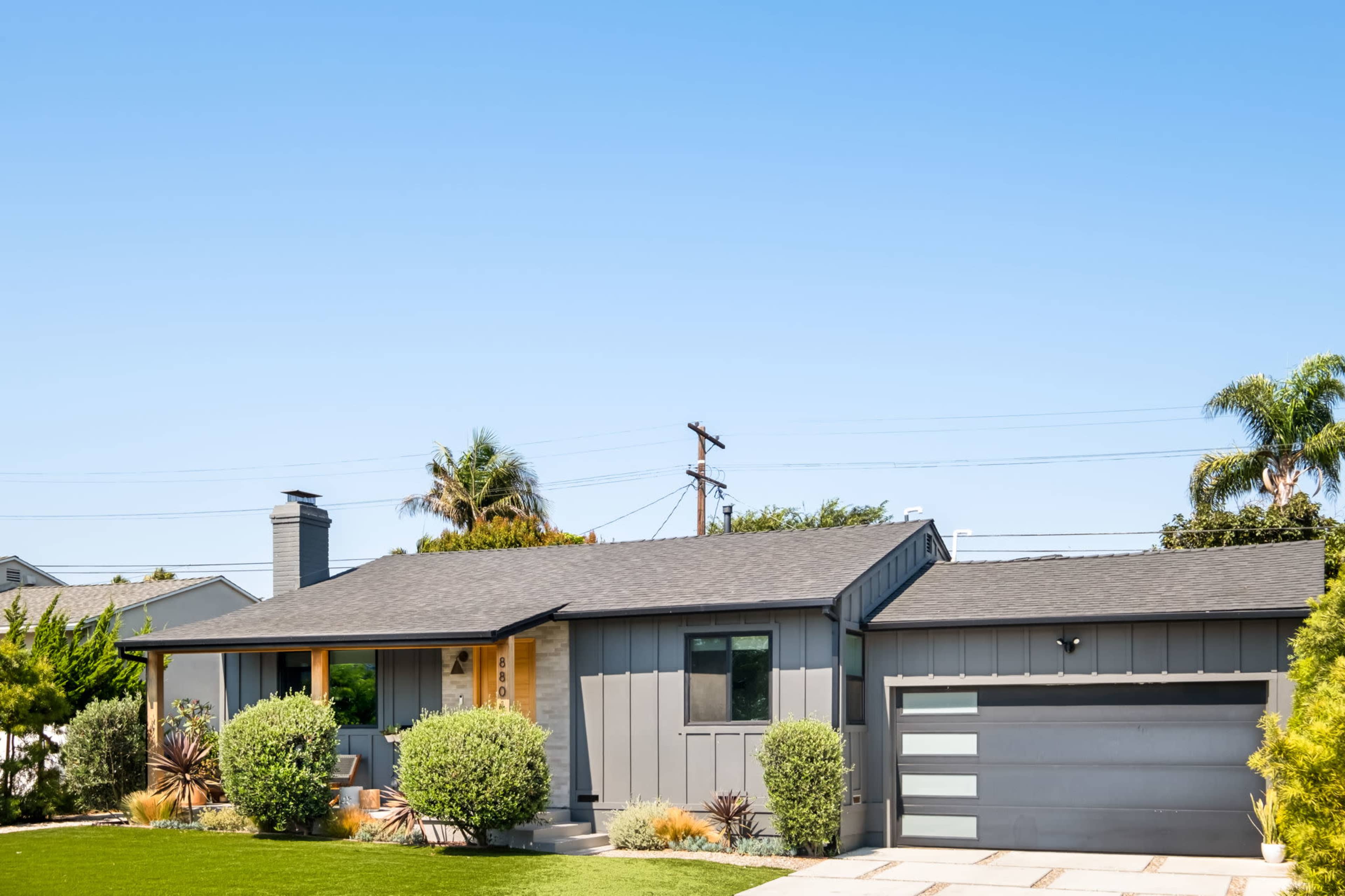 A modern single-story house with a dark exterior and a manicured front lawn features a garage on the right side.