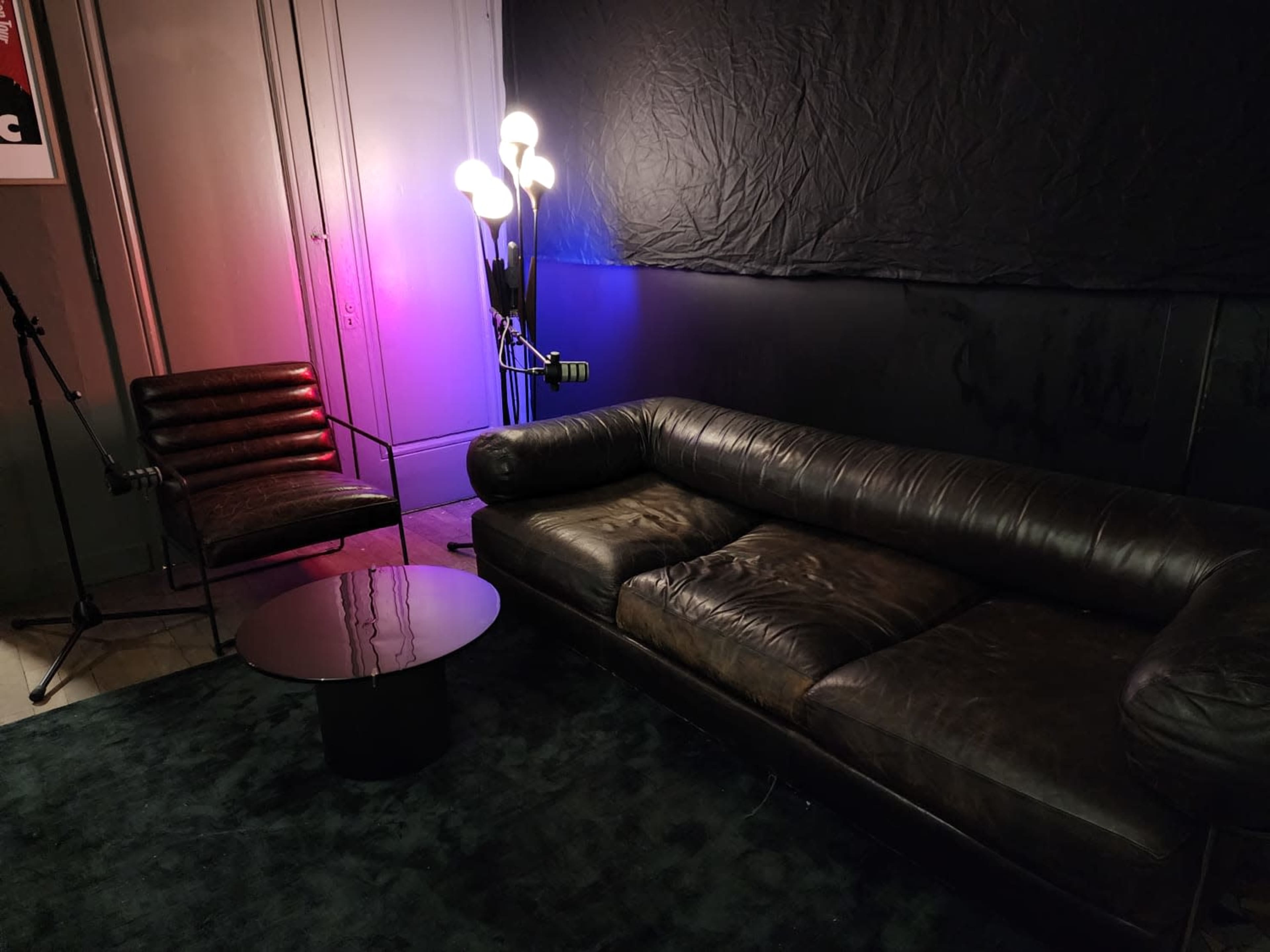 The scene features a dark room with a leather sofa, a modern chair, a round table, and a lamp with multiple light bulbs illuminating the space.