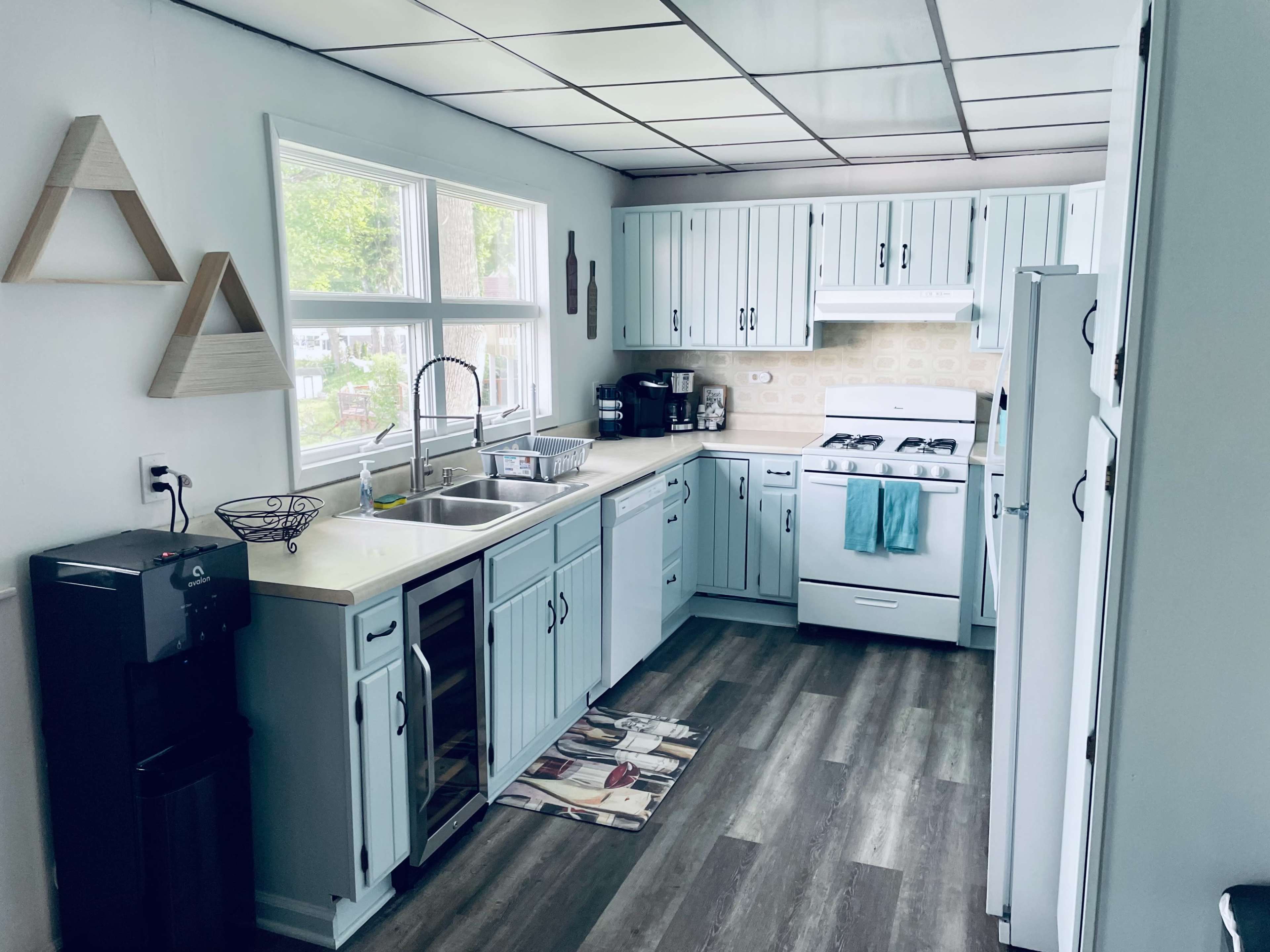 A kitchen with light blue cabinets, a sink, a stove, and a refrigerator, featuring a small dining mat on the floor.