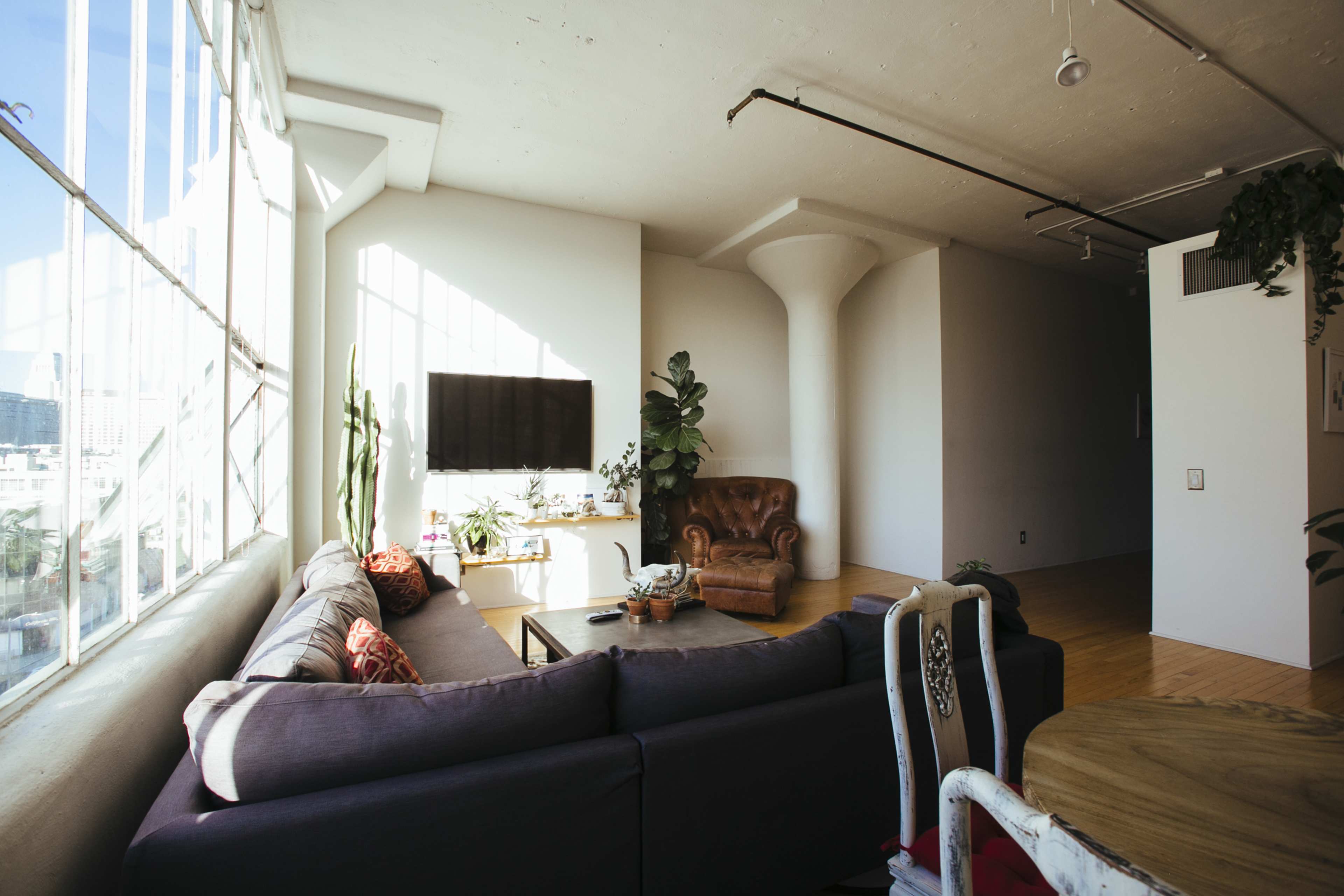 A modern living room features a large sectional sofa, a wooden coffee table, and a wall-mounted TV beside floor-to-ceiling windows that let in natural light.