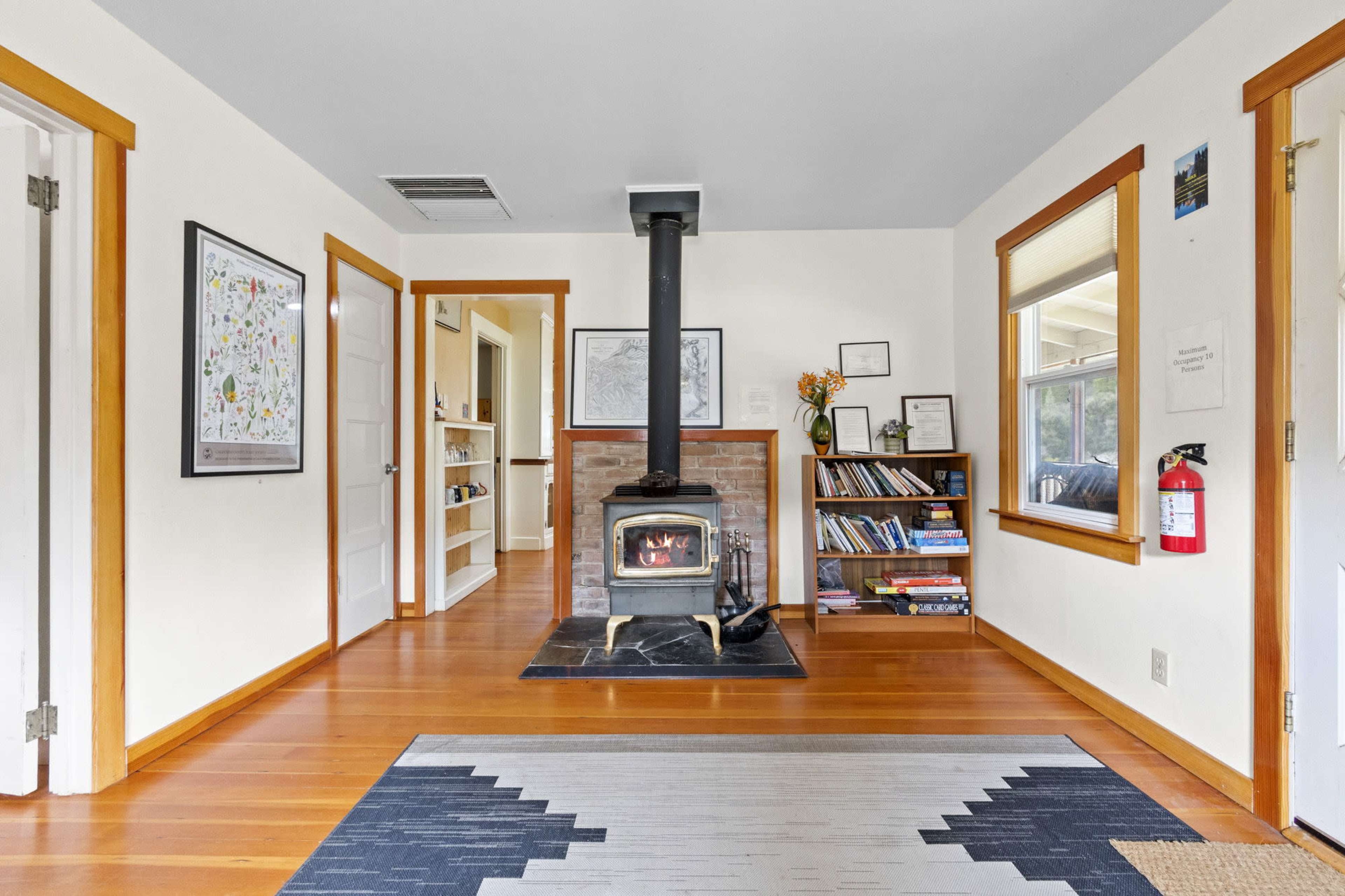 A cozy room with a wood stove on a brick pedestal, wooden floors, and shelves filled with books along one wall.