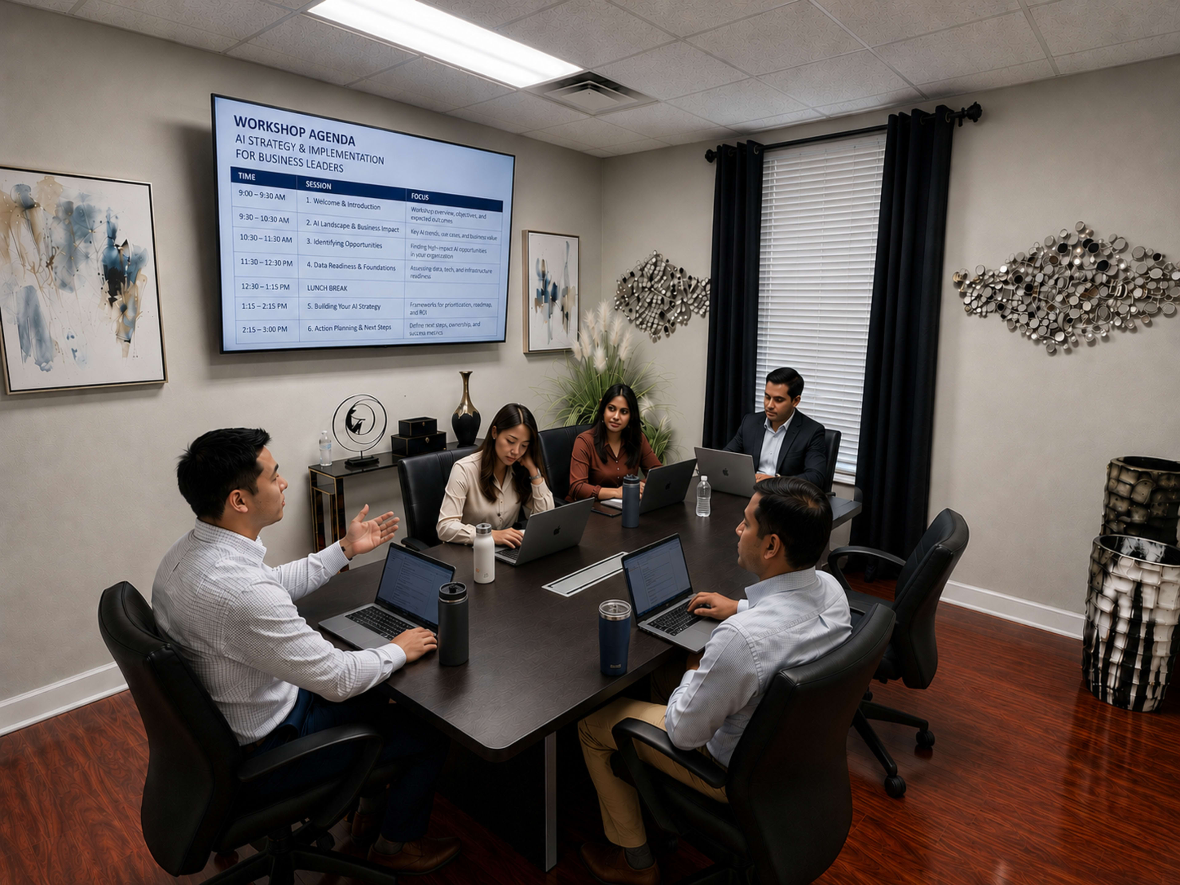A group of five professionals is seated around a conference table in a meeting room with a workshop agenda displayed on a screen.