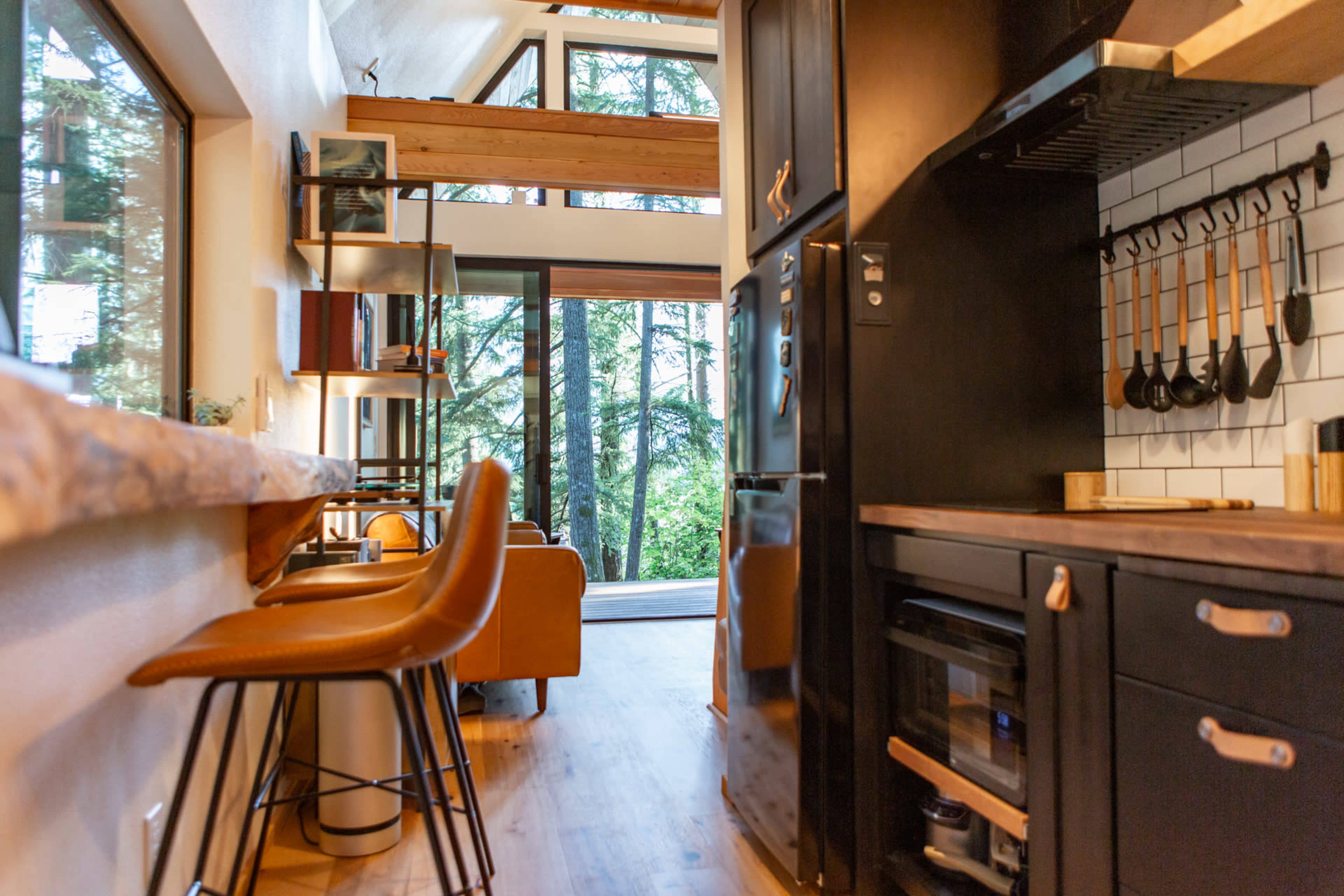 The interior of a modern kitchen and living area with a large window overlooking a forest.