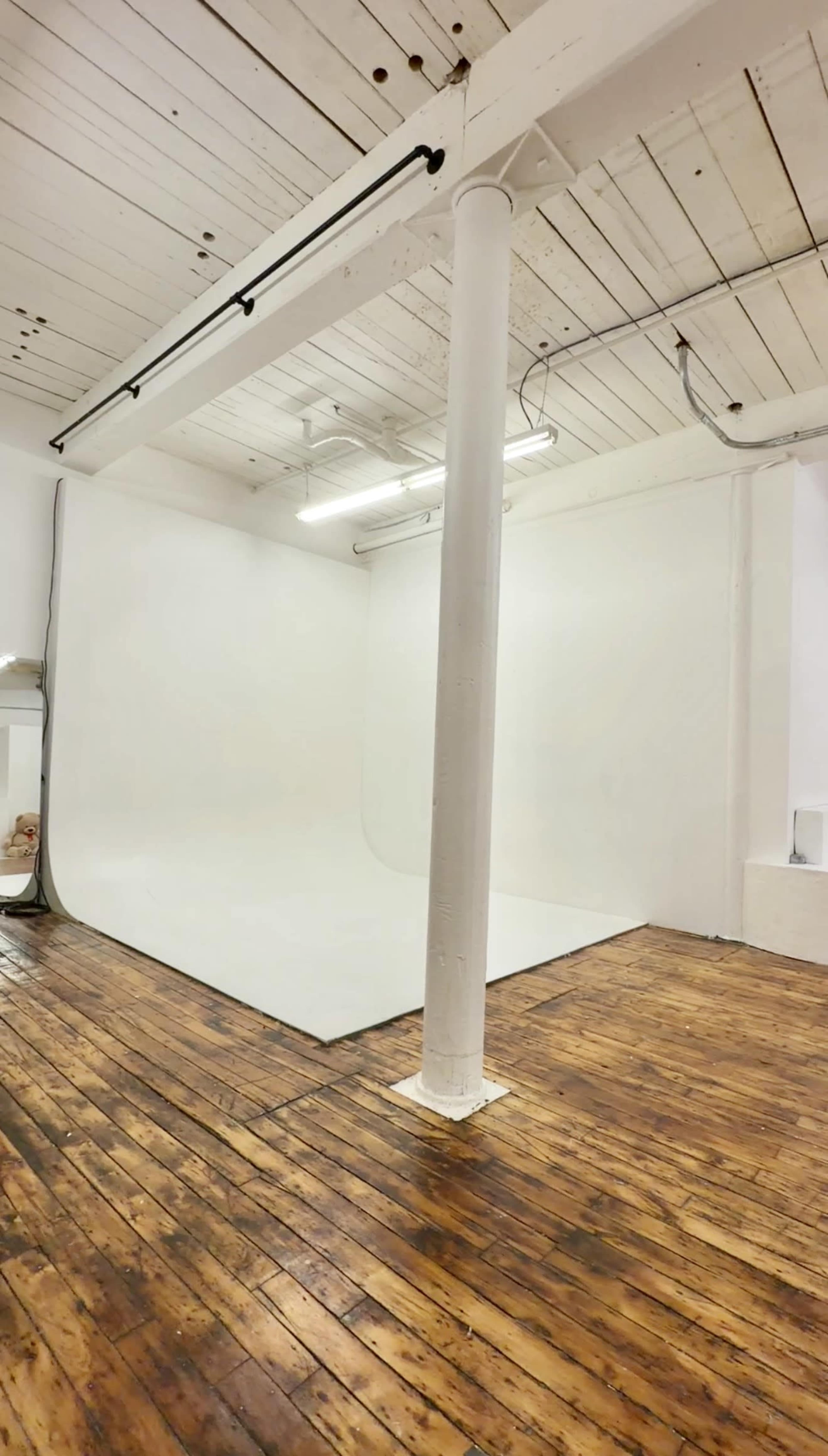 The image shows a spacious photography studio with a white backdrop and wooden flooring.