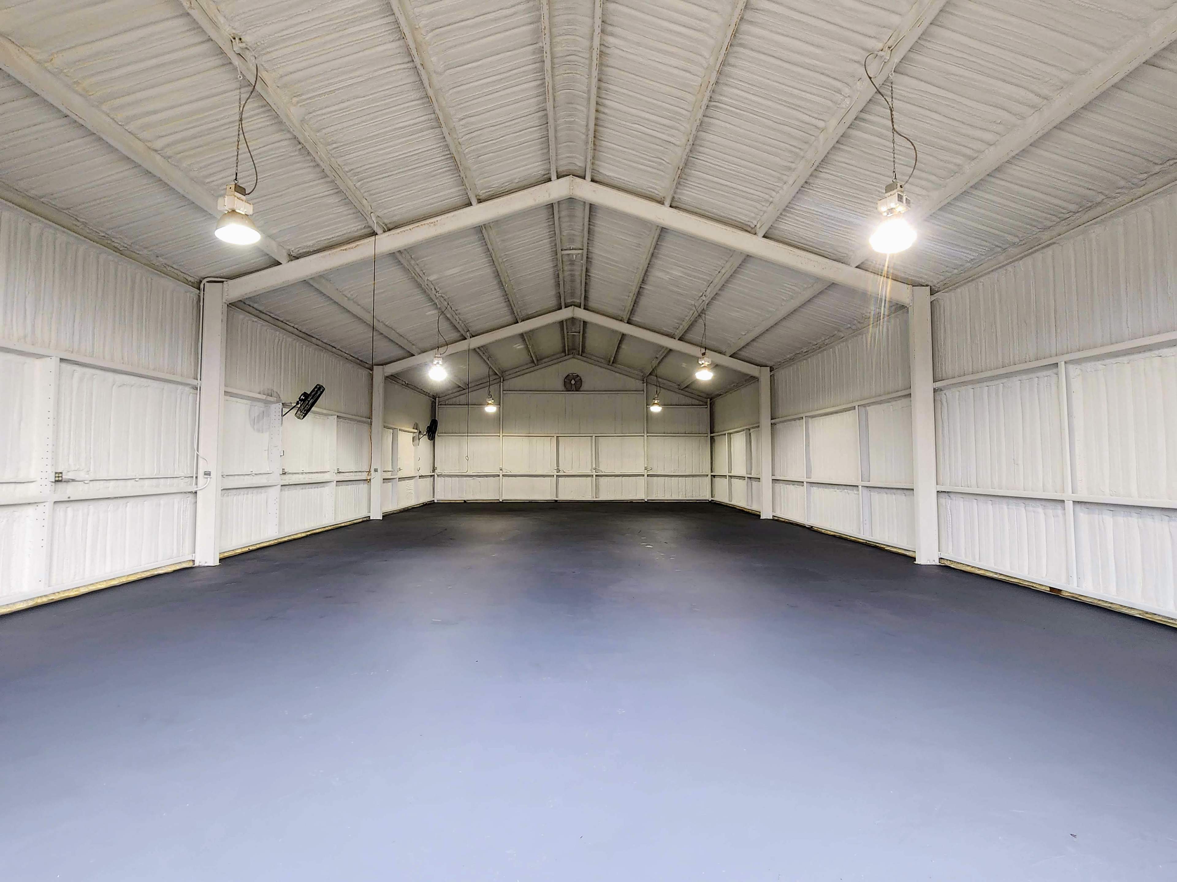 A large, empty warehouse with a high ceiling and concrete floor, illuminated by overhead lights.