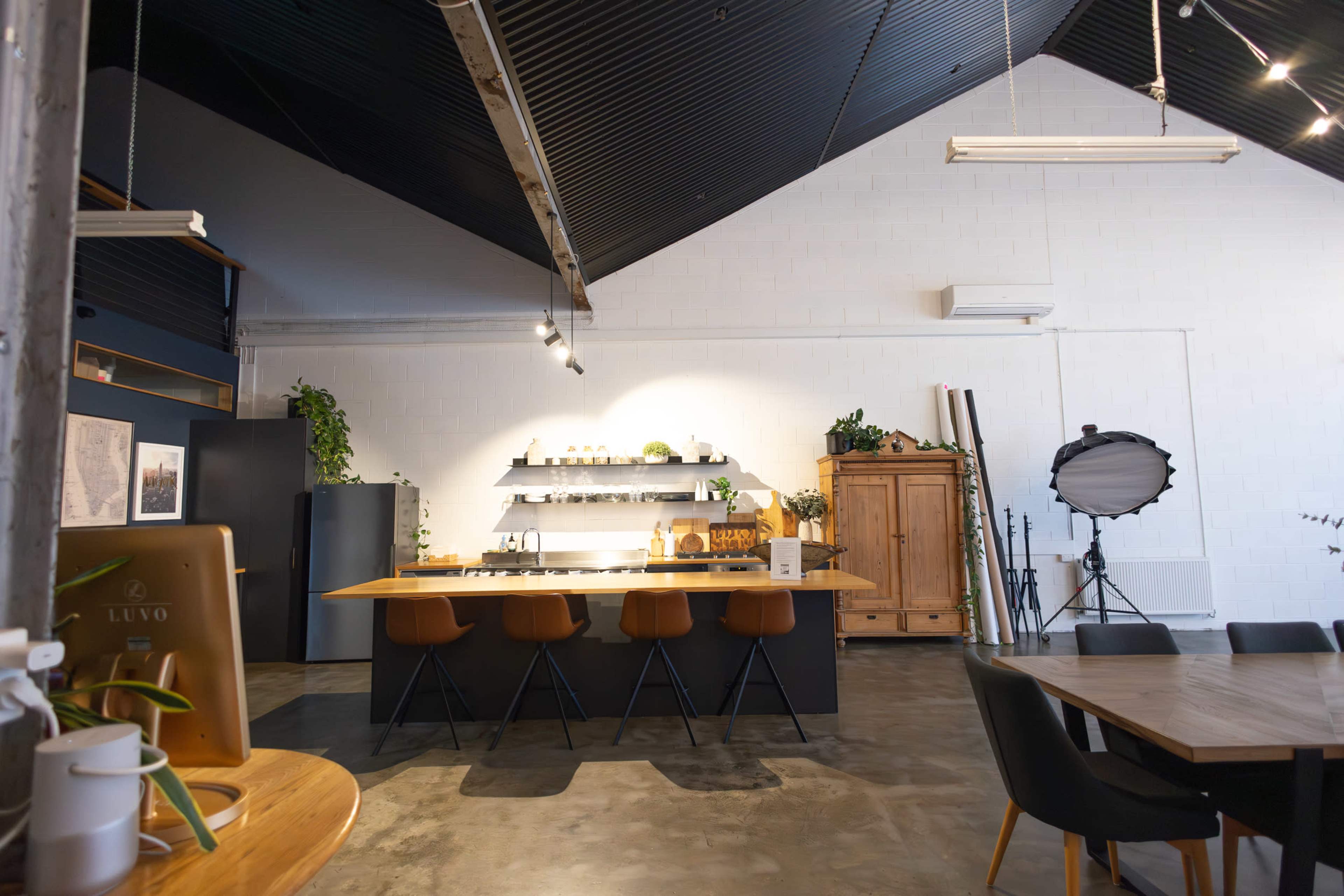 The image shows a modern kitchen and dining area with an island counter, sleek cabinetry, and wooden dining furniture under a high, angled ceiling.