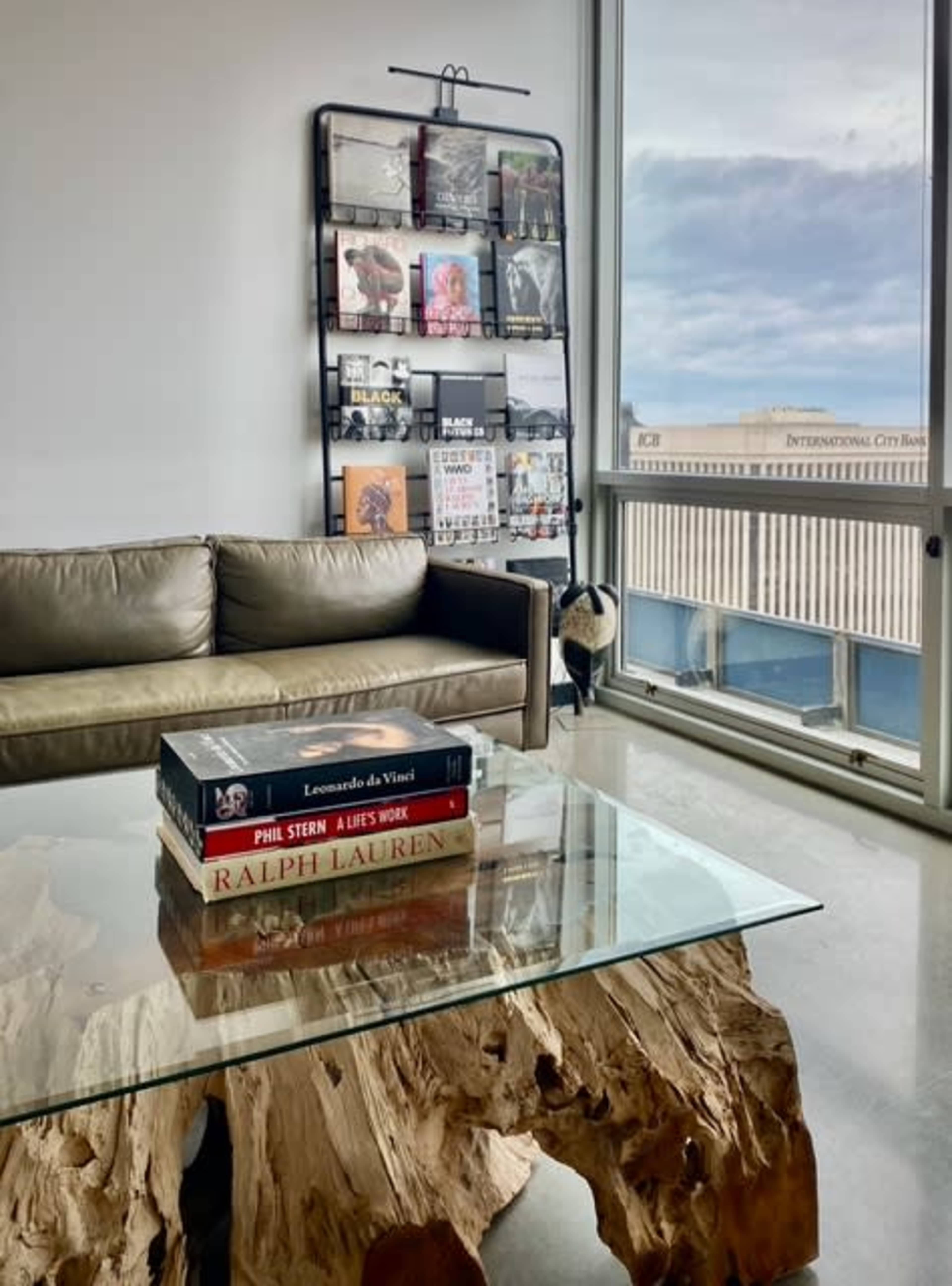 A modern living area with a leather sofa, a glass coffee table made from a wood slab, and a wall-mounted magazine rack filled with various publications.