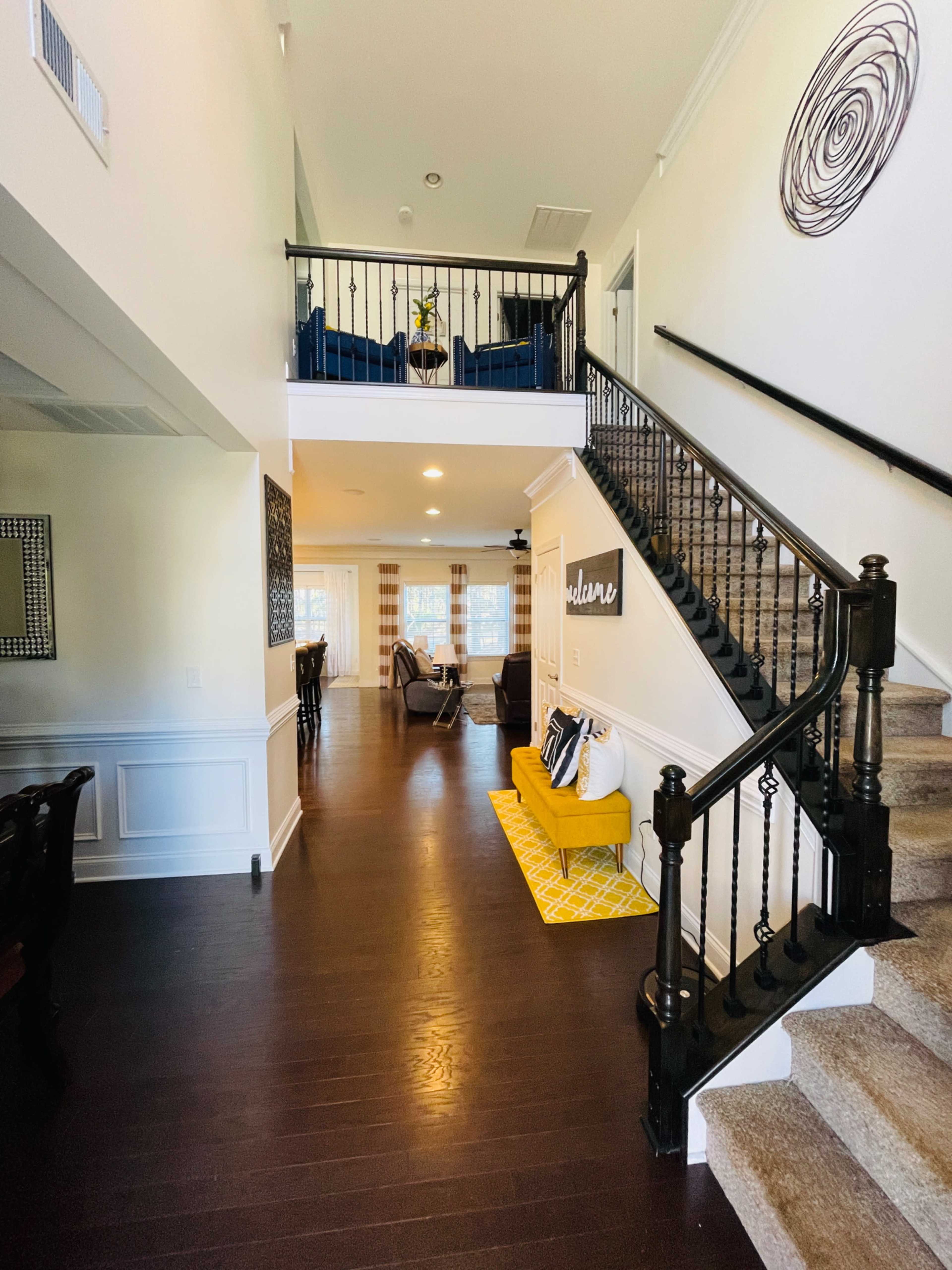 A two-story foyer with a staircase, a yellow bench, and seating areas visible on both levels.