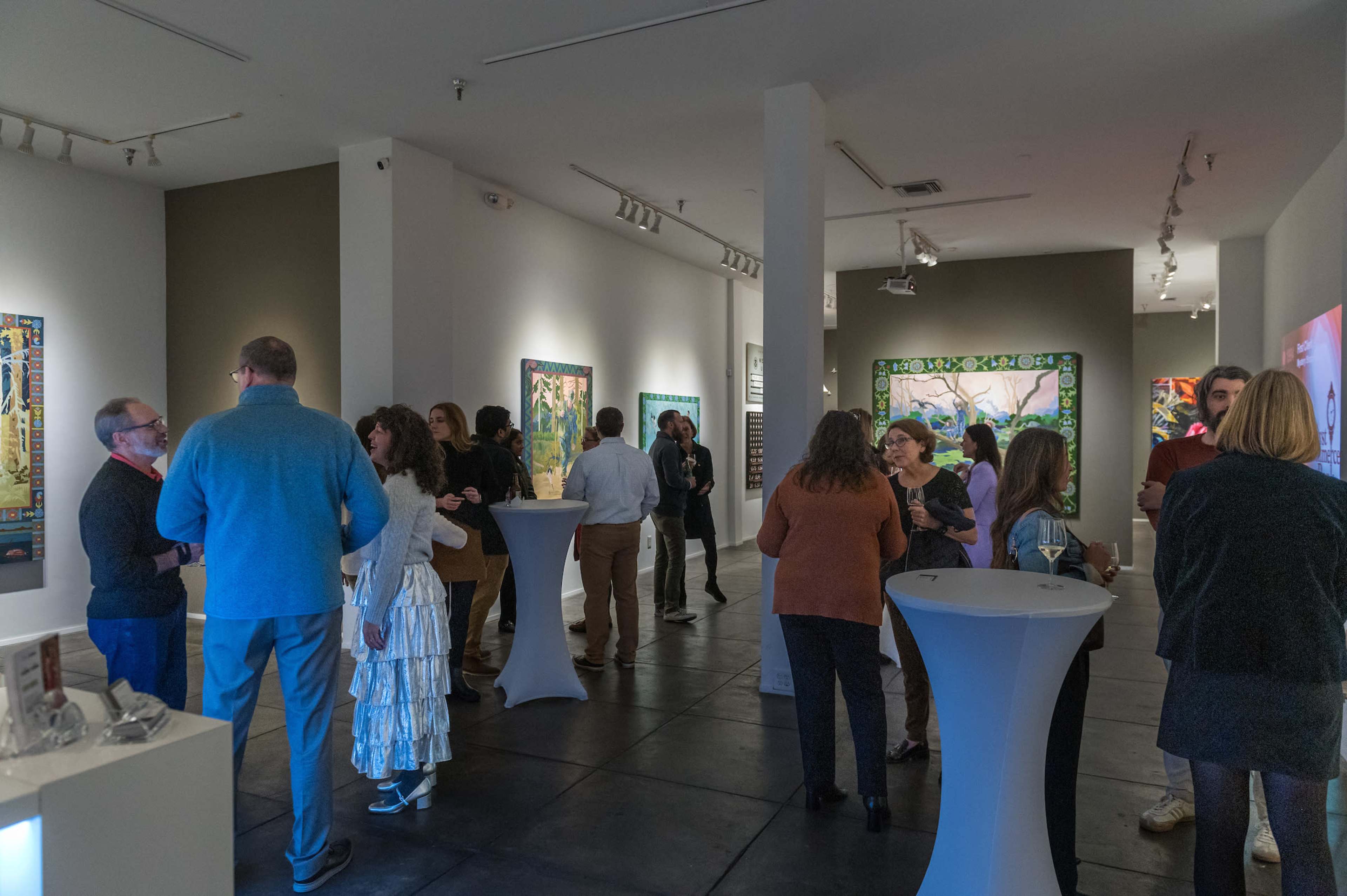 A group of people is mingling at an art gallery opening, surrounded by colorful artworks on the walls.