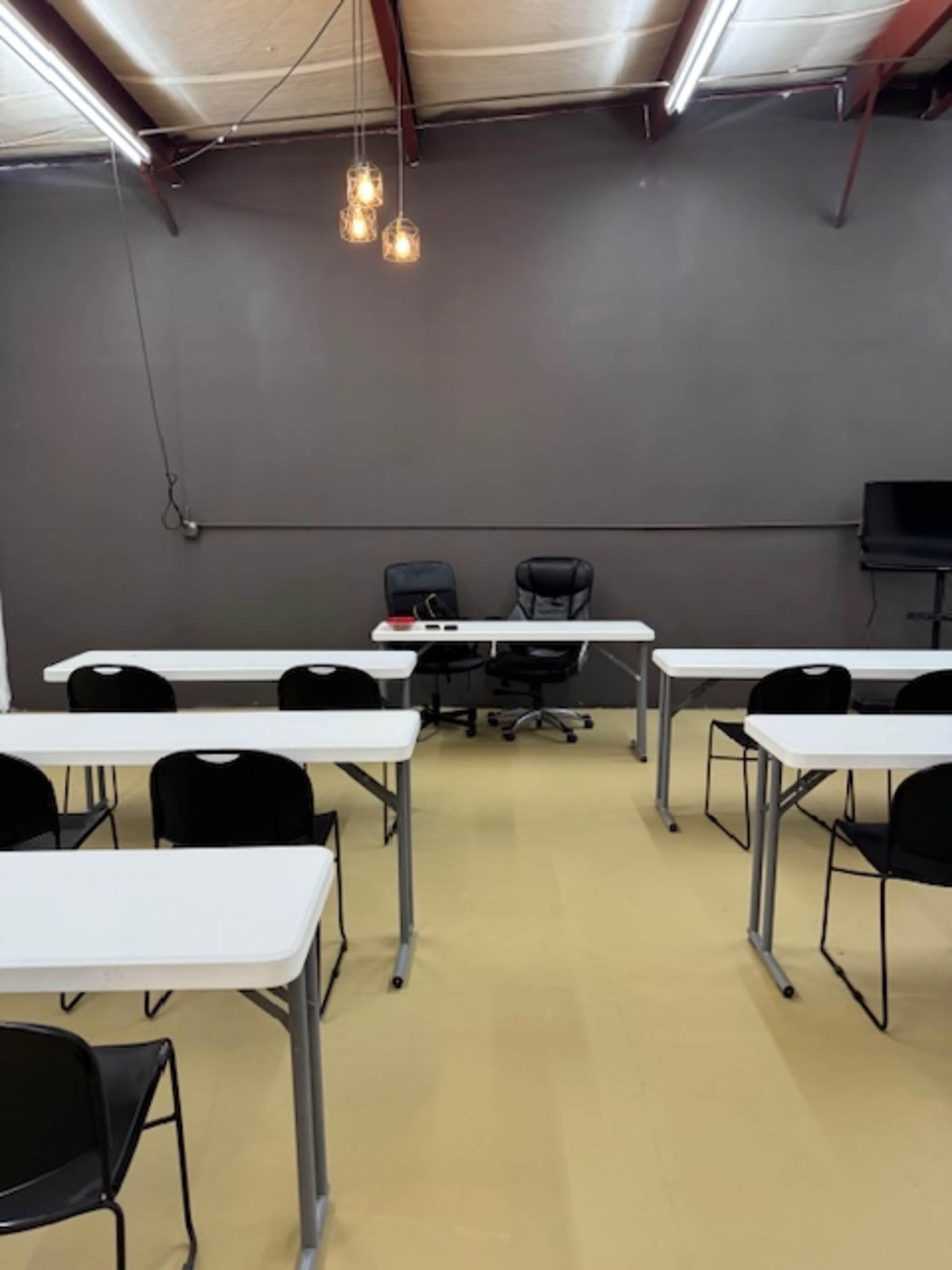 The image shows a classroom setting with rows of desks and two office chairs positioned at the front.