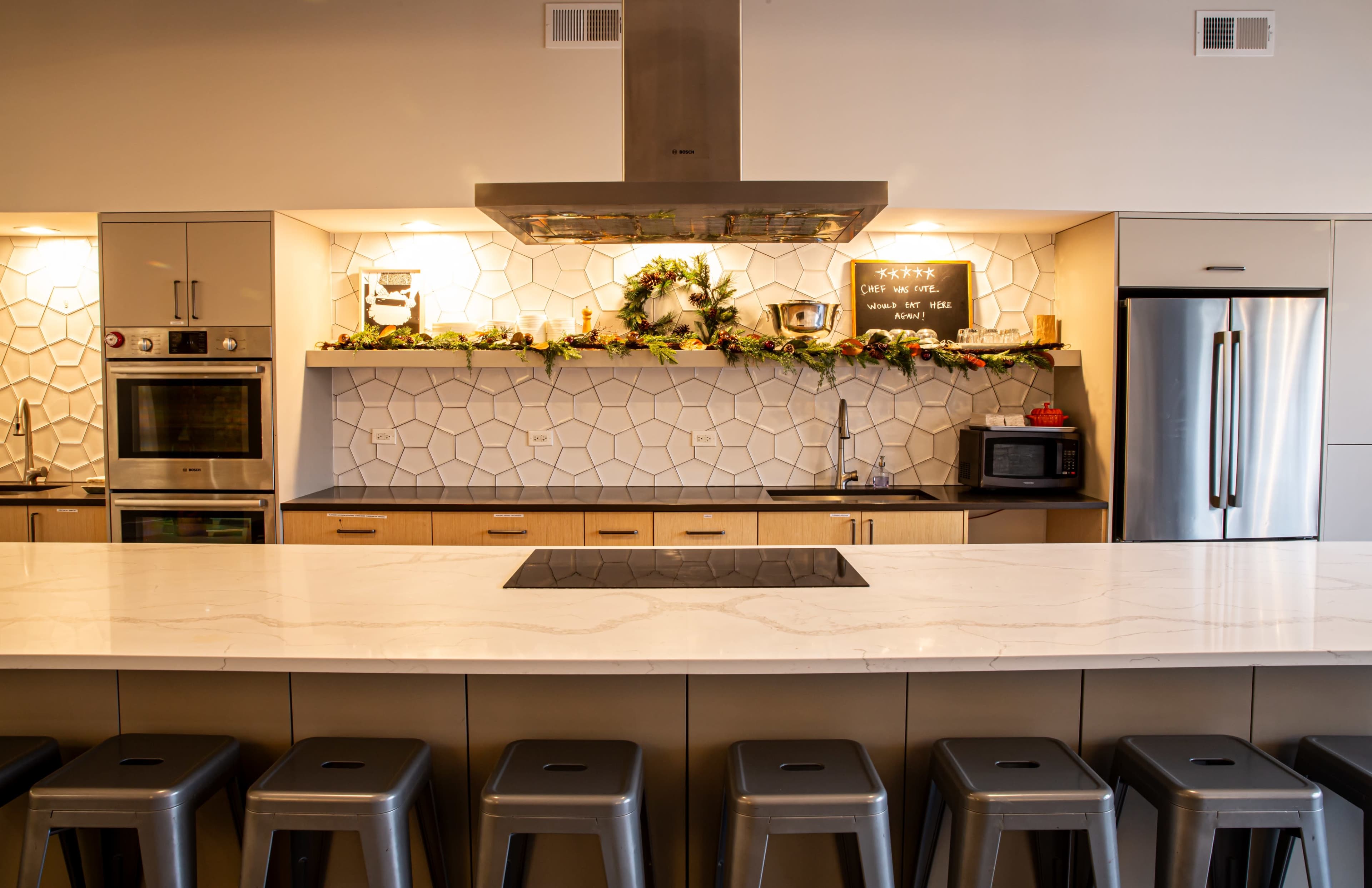A modern kitchen with a large island and bar seating, featuring sleek cabinetry, a decorative backsplash, and stainless steel appliances.