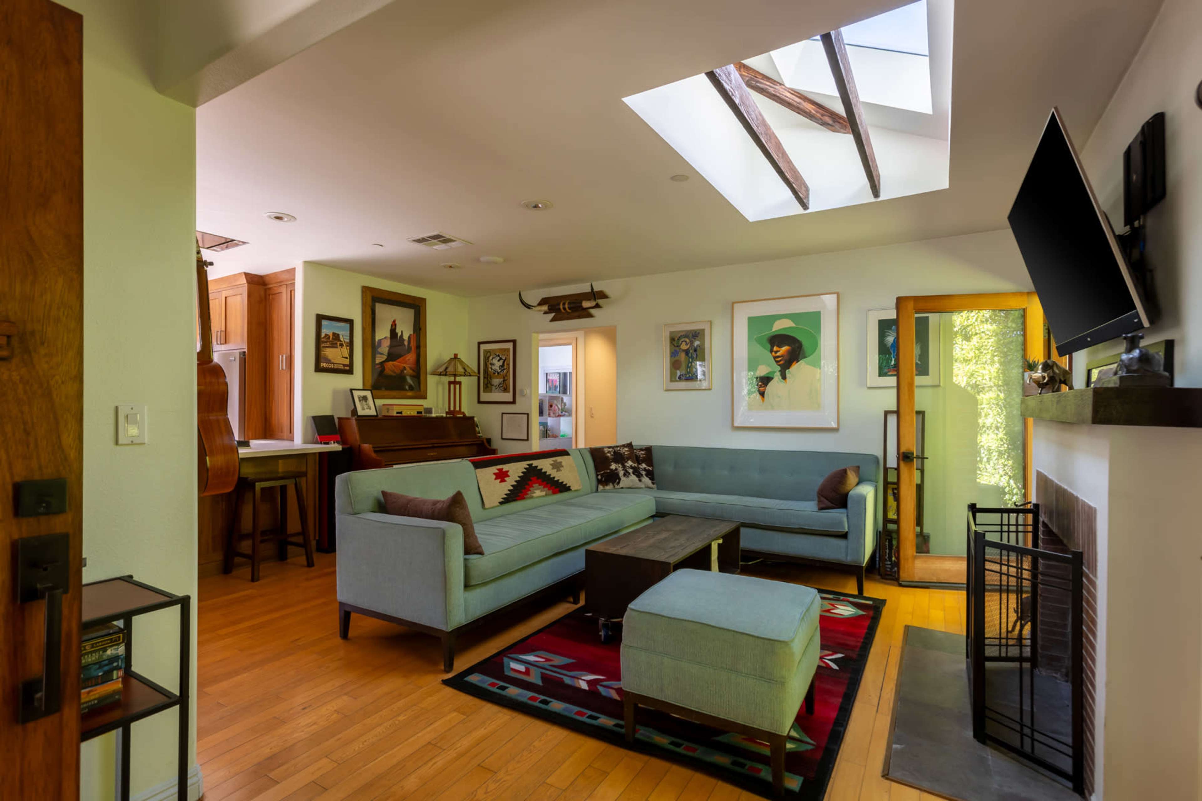 The image shows a cozy living room with a sectional sofa, wooden flooring, and a skylight illuminating the space.