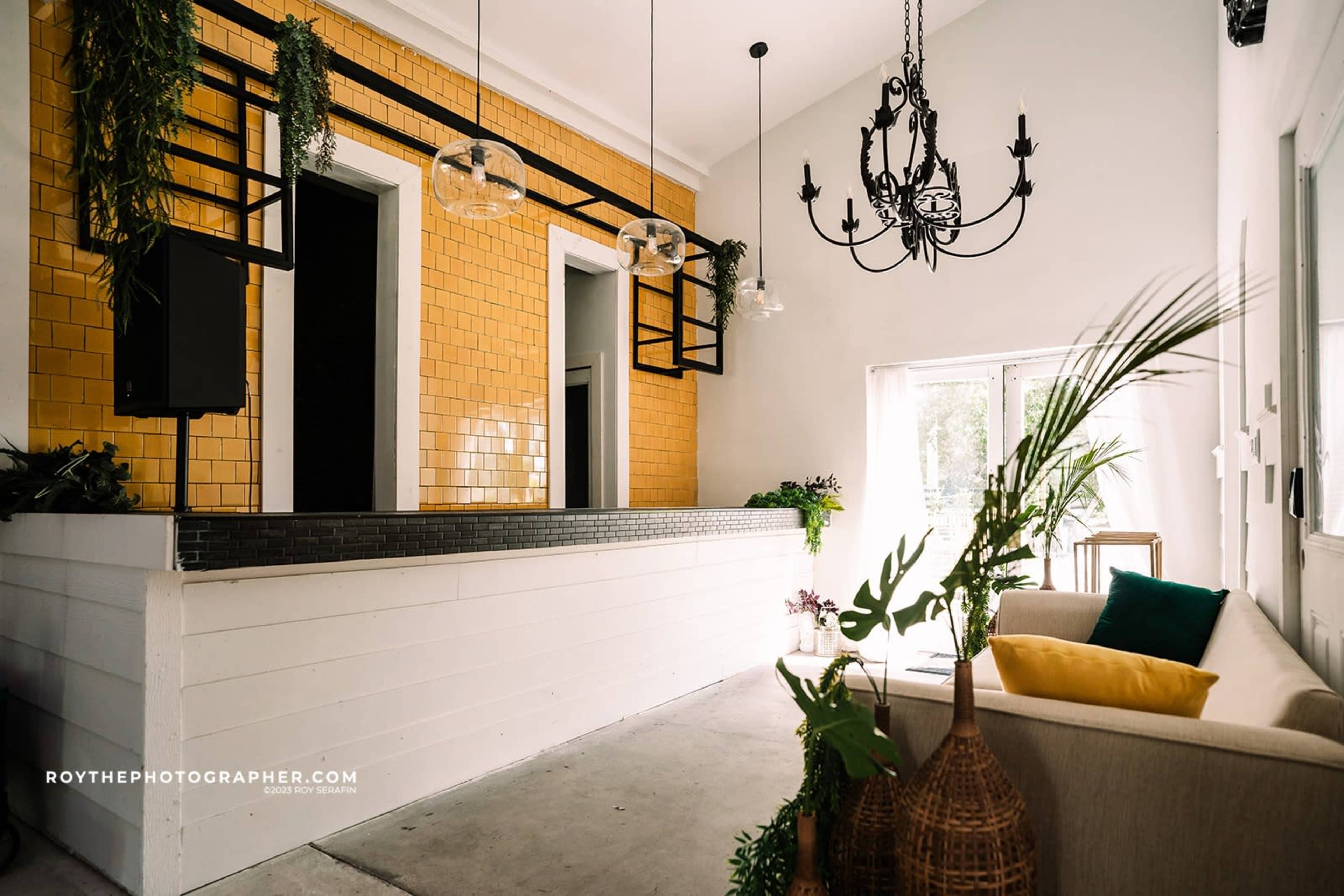 A welcoming reception area featuring a yellow tiled wall, a modern chandelier, and a sofa with decorative pillows.