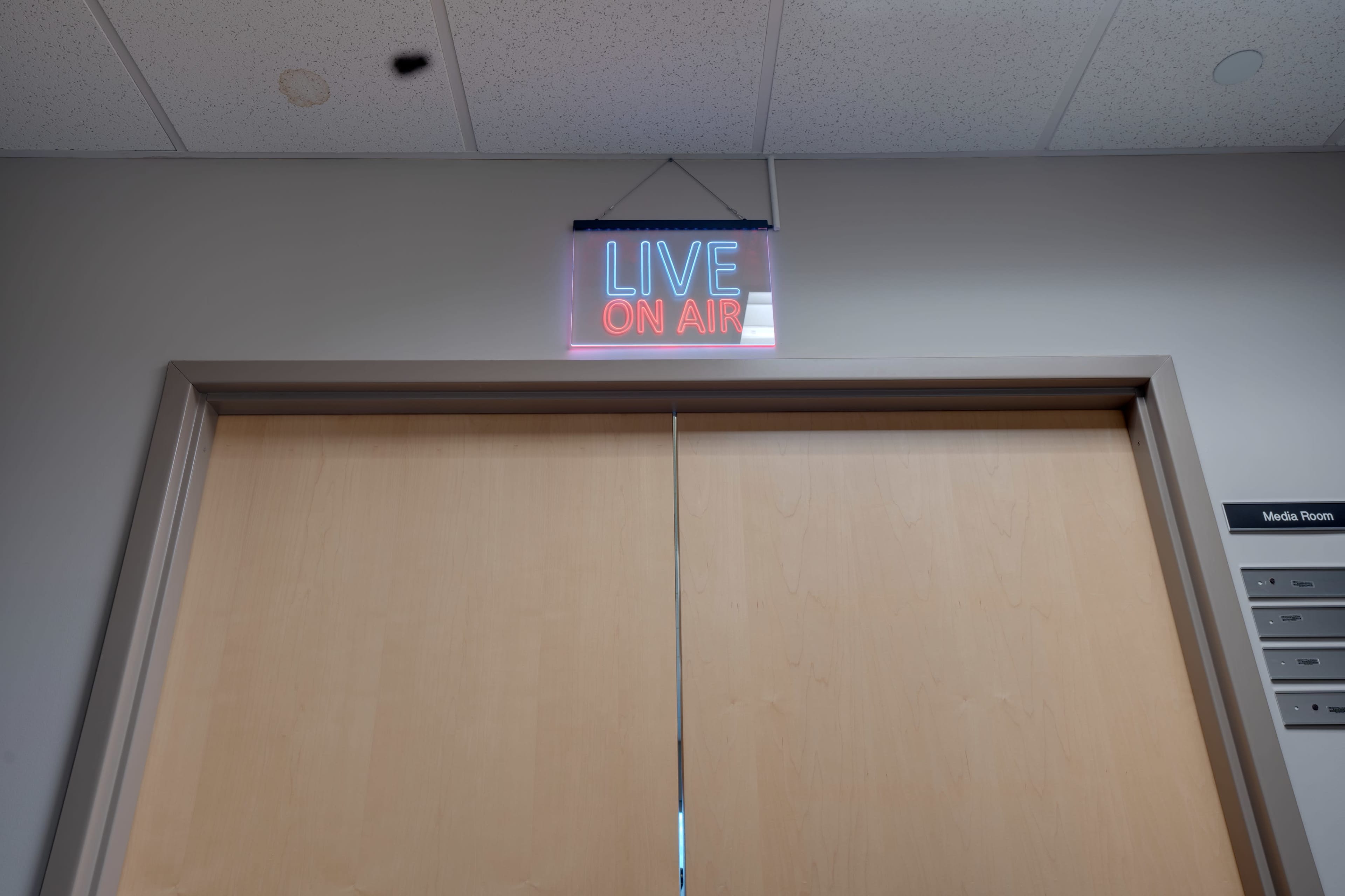 A neon sign labeled "LIVE ON AIR" is illuminated above a closed wooden door.