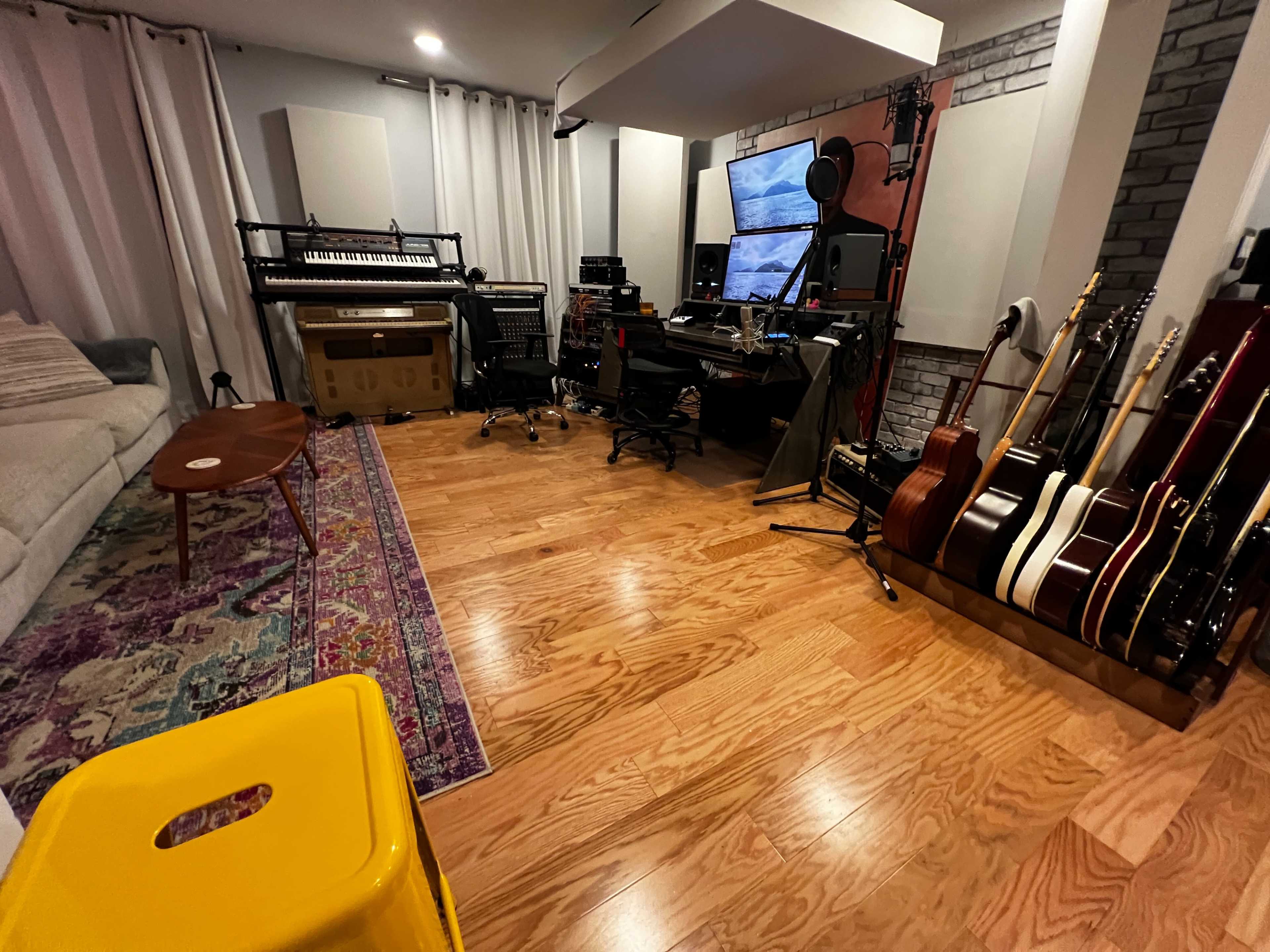 The image shows a music studio featuring various musical instruments, recording equipment, and a comfortable seating area with a vibrant rug.