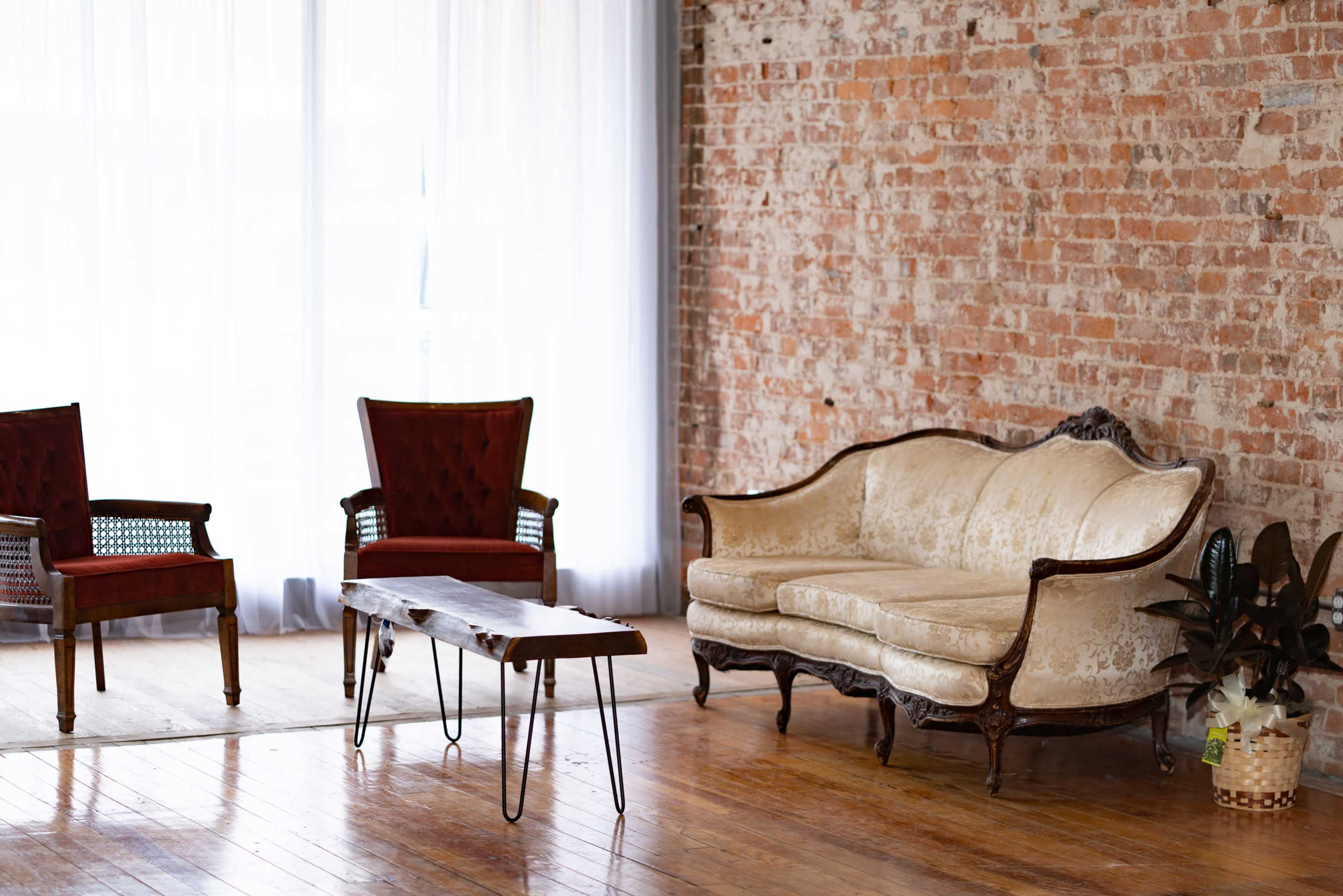 A cozy interior setting with a vintage sofa, two red upholstered chairs, a wooden coffee table, and brick walls.