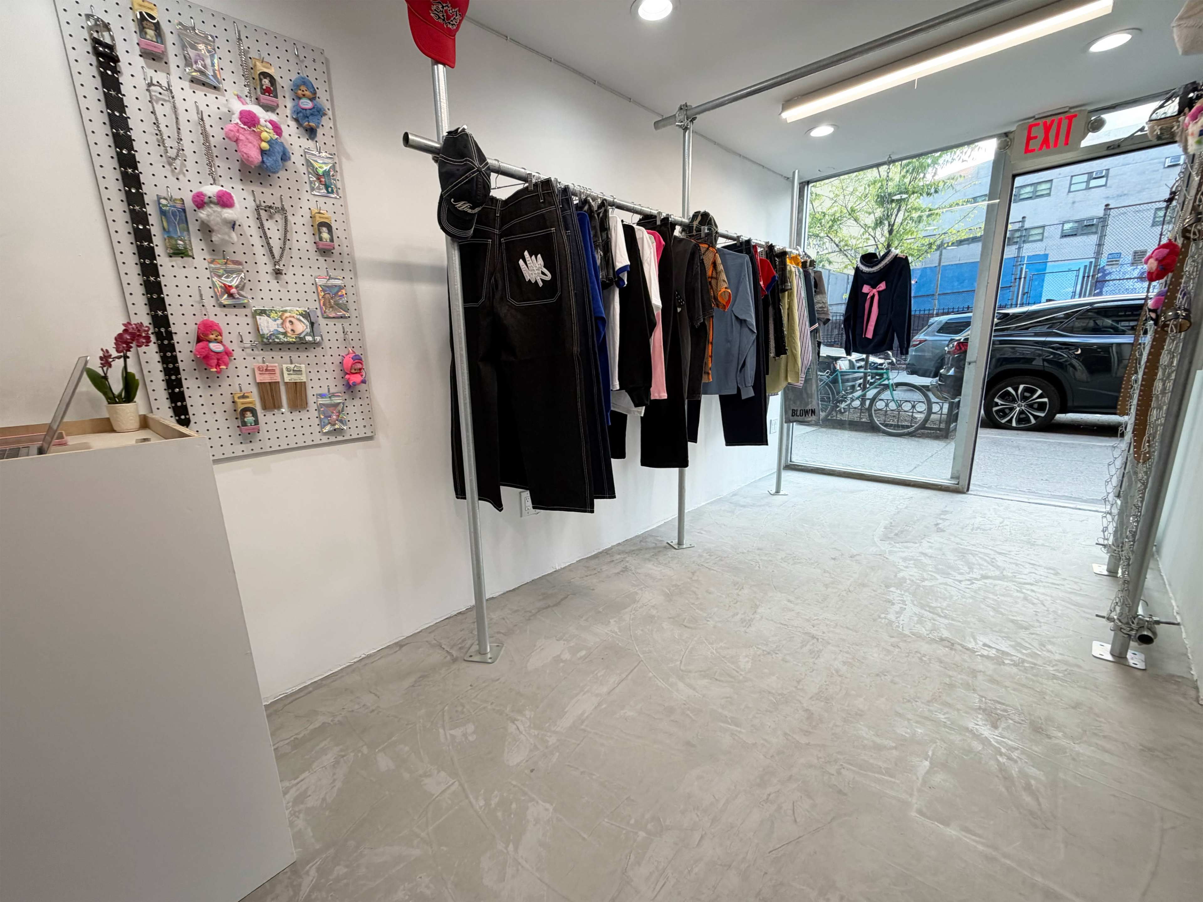 The image shows a clothing retail space with a display rack of various garments and a large window facing the street.