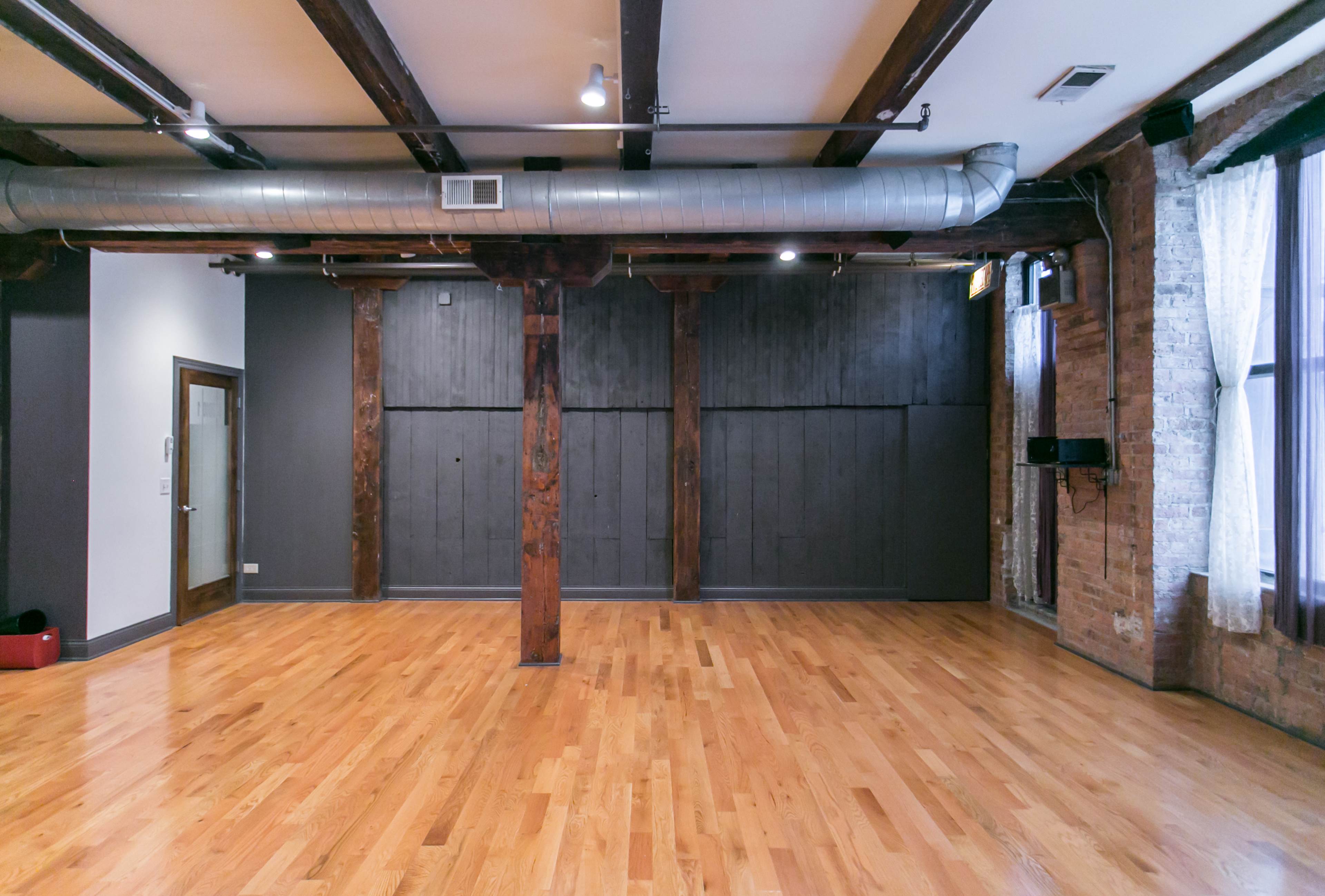 A spacious room with exposed wooden beams, hardwood flooring, and a large window allowing natural light to enter.