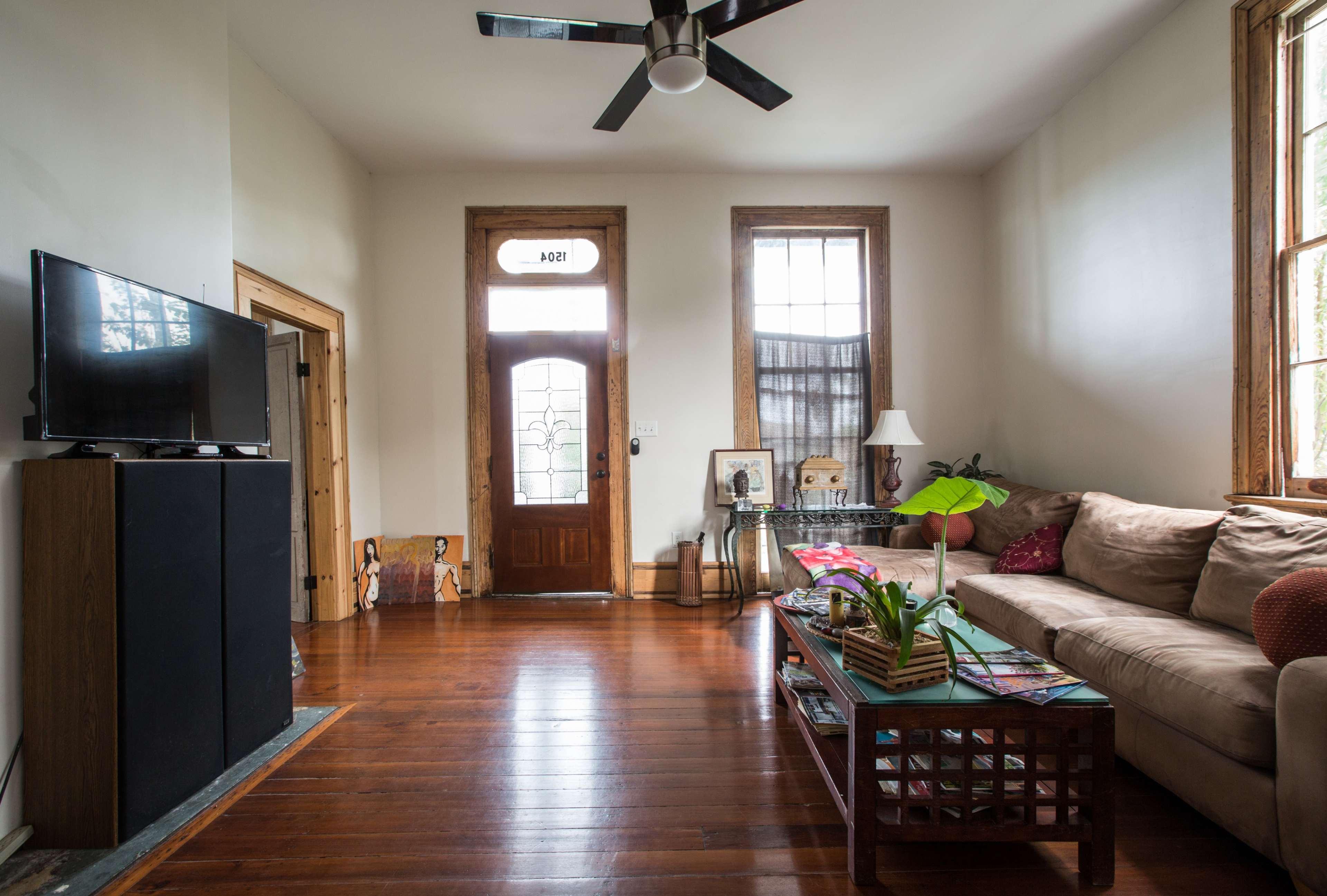 The image shows a living room with a beige sofa, a wooden coffee table, a television on a black cabinet, and a door with large windows.