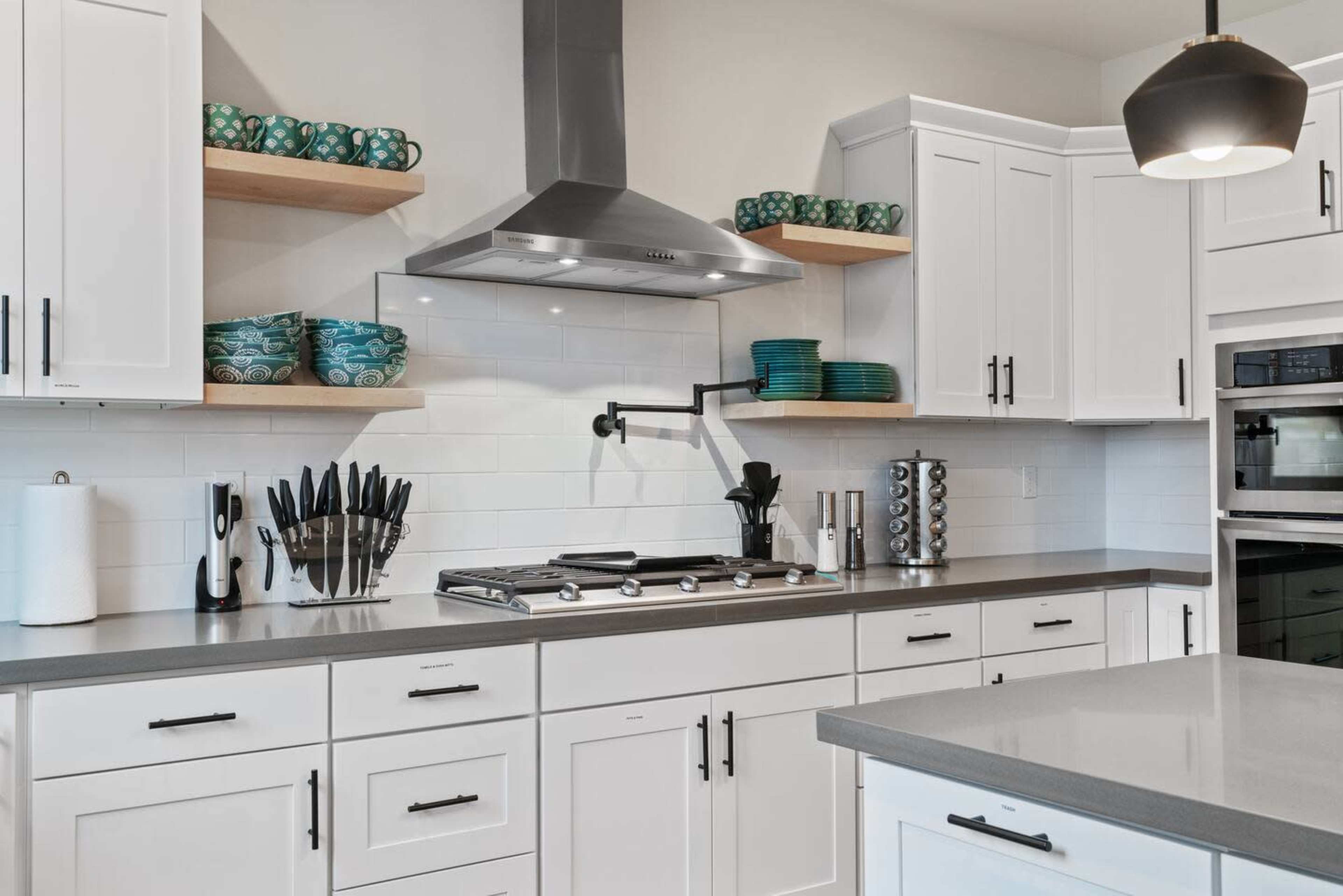 A modern kitchen features white cabinetry, stainless steel appliances, and open shelving displaying colorful dishware.
