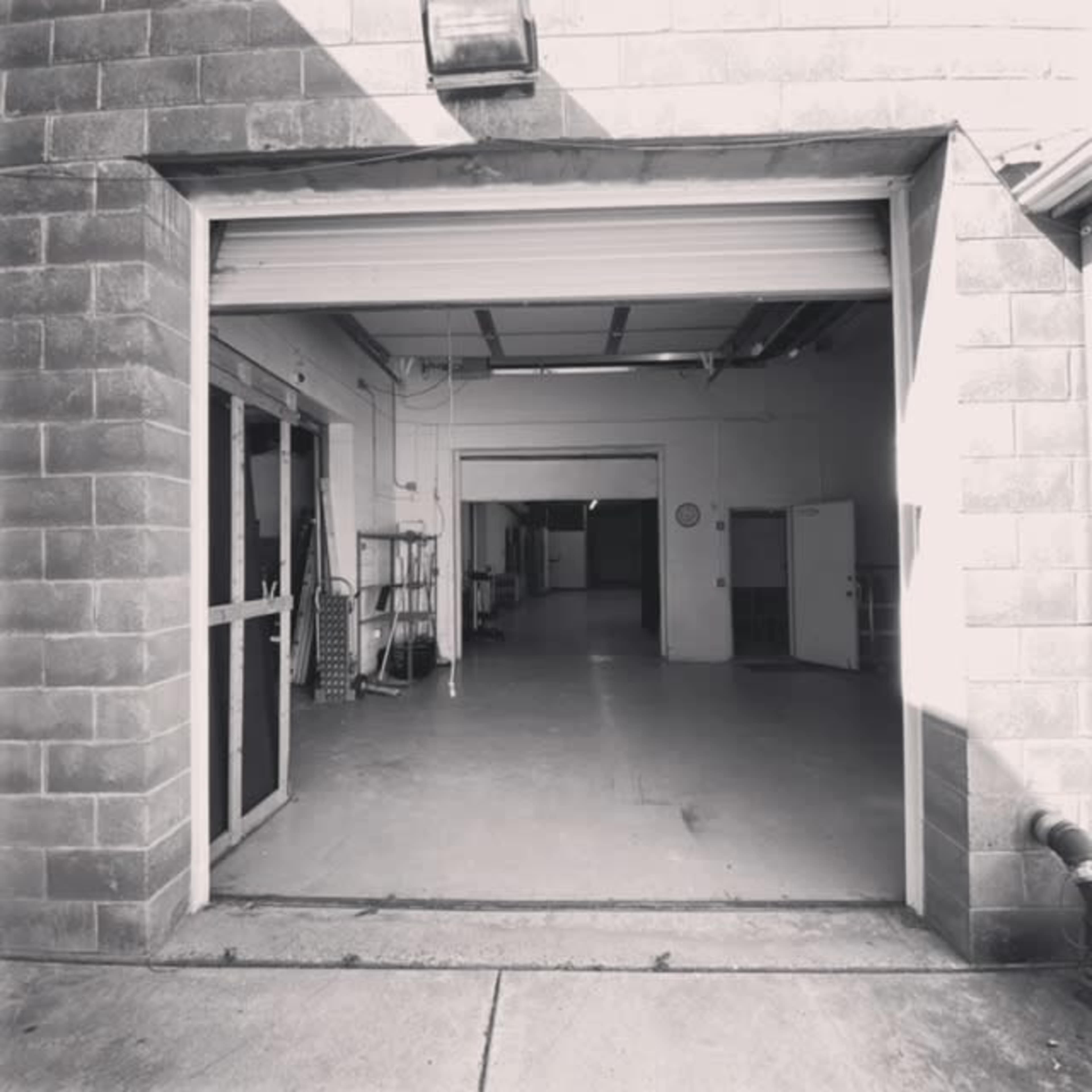 An open garage door leading into a large, empty industrial space with concrete flooring and several doors on the walls.