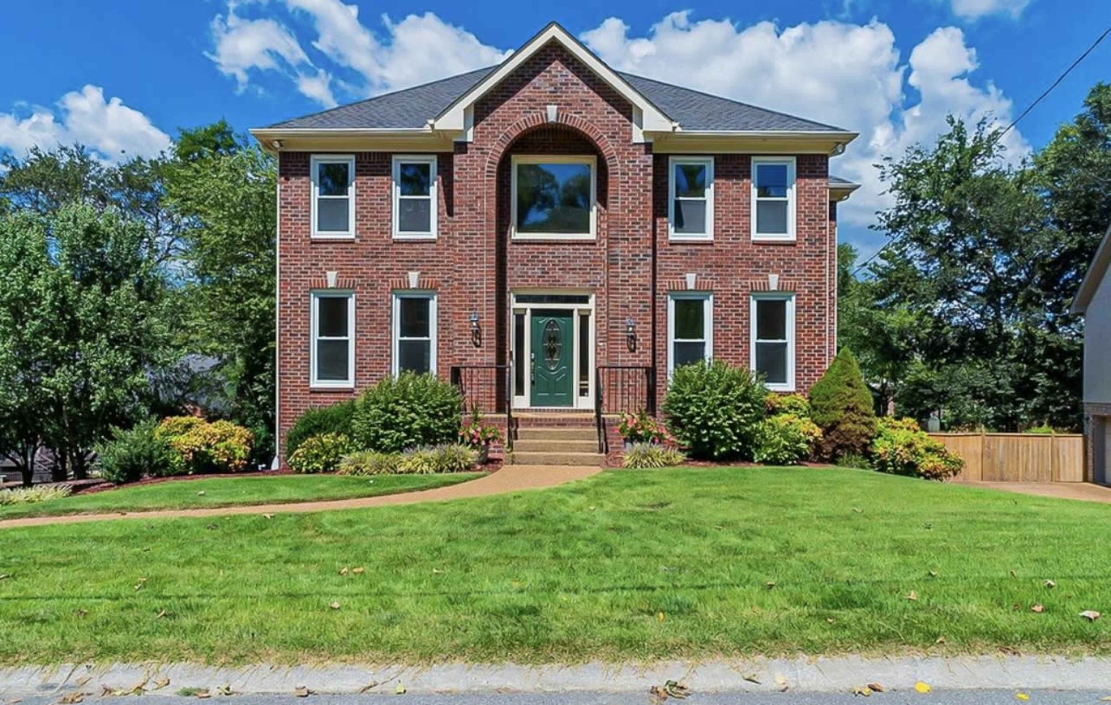 A large brick home with multiple windows and a symmetrical facade sits on a well-maintained lawn.