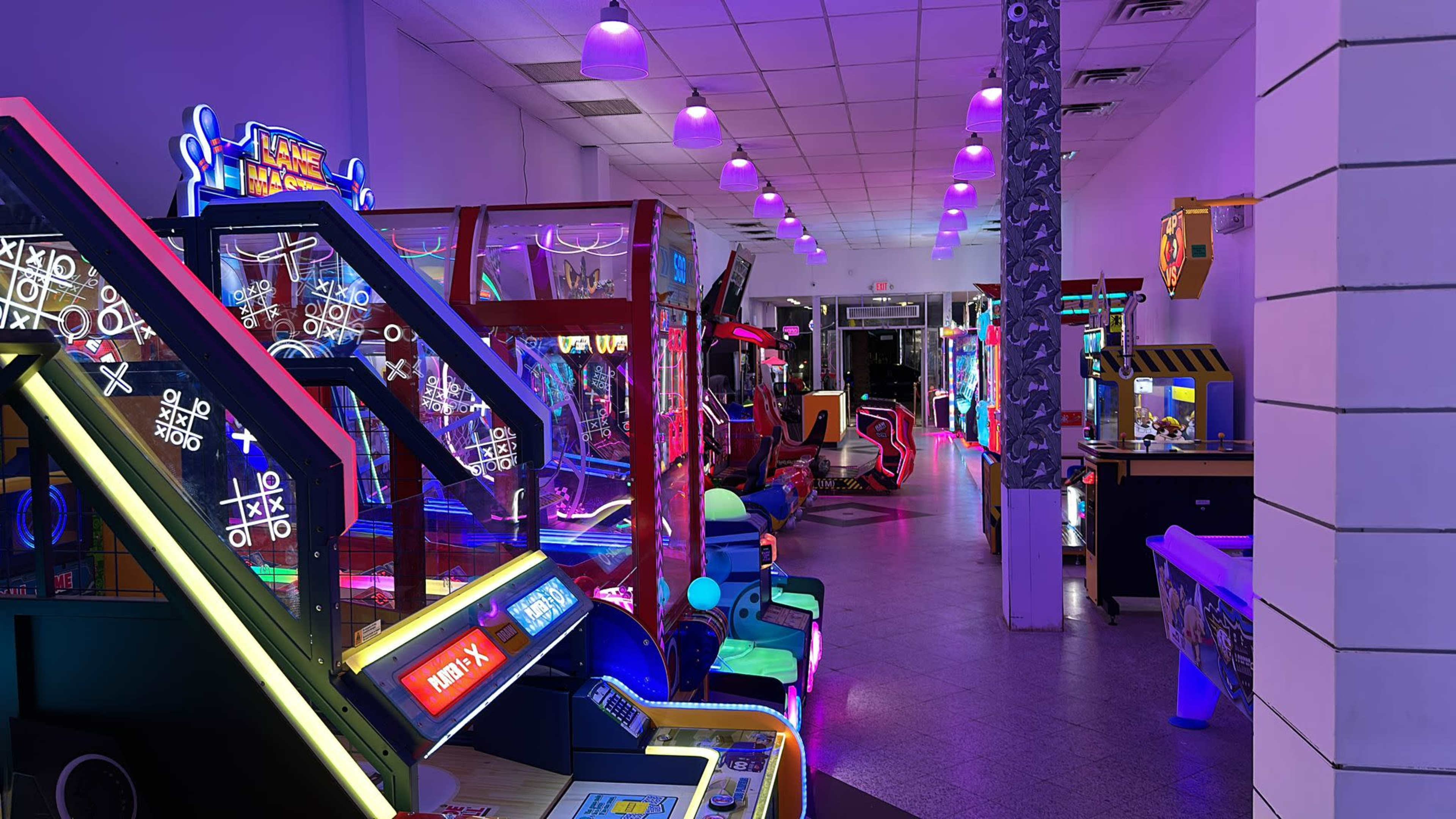 The image shows a brightly lit arcade filled with various gaming machines and neon lights, creating a vibrant atmosphere.