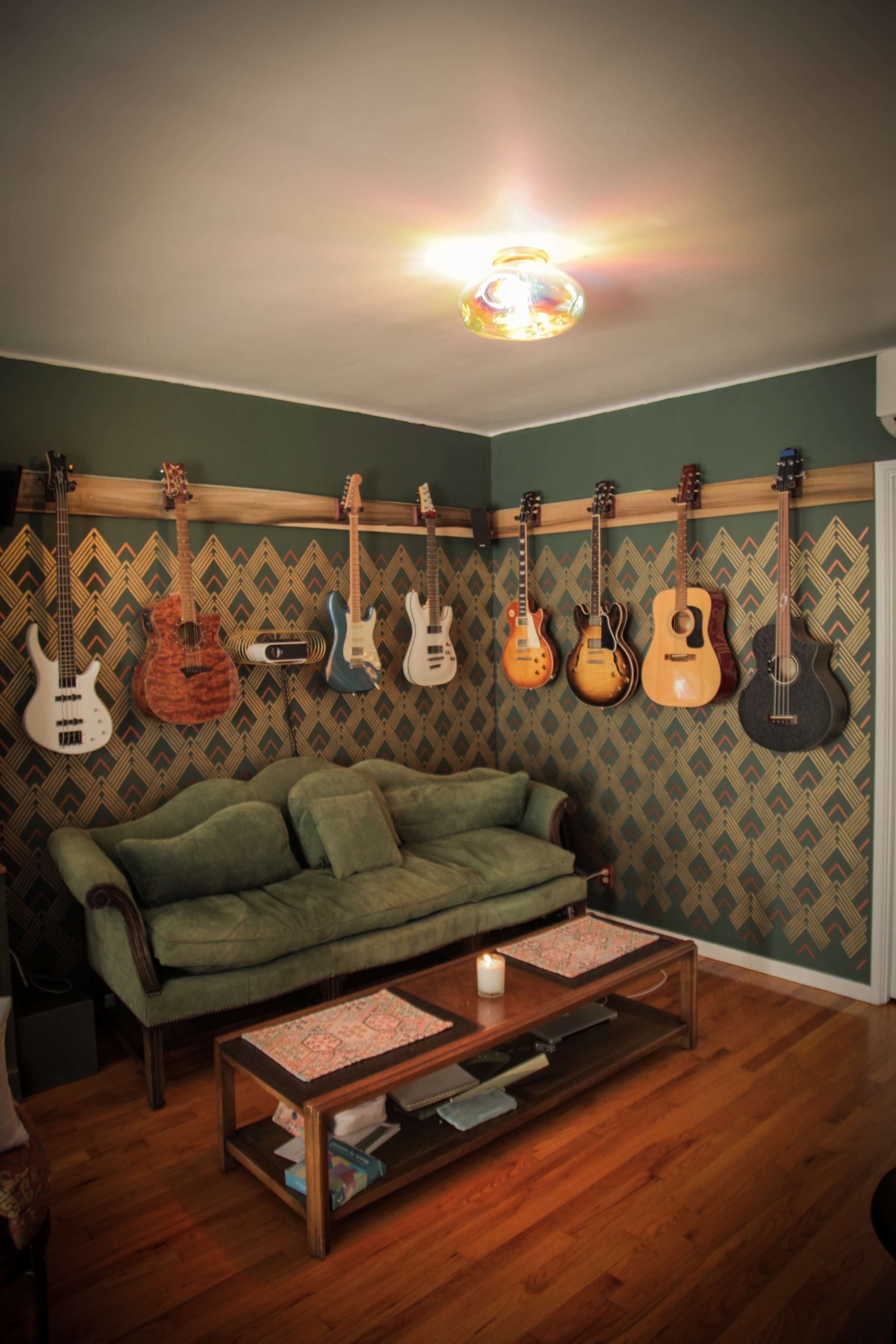 A cozy living room with a green couch, a low wooden coffee table, and several guitars hanging on the wall against a patterned wallpaper.