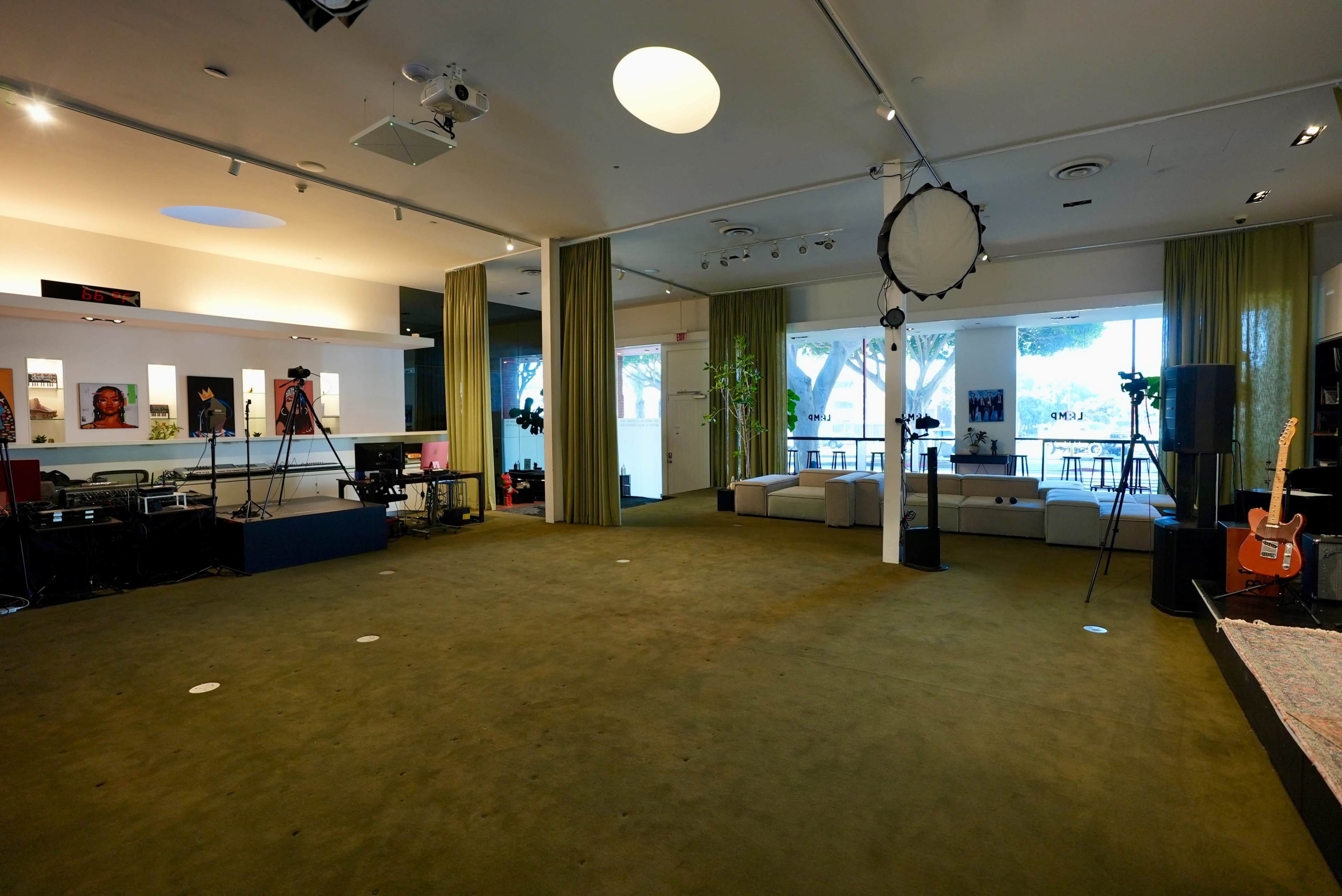 The image shows a spacious indoor area with a green carpet, several seating arrangements, musical instruments, and photography equipment set up for a creative environment.