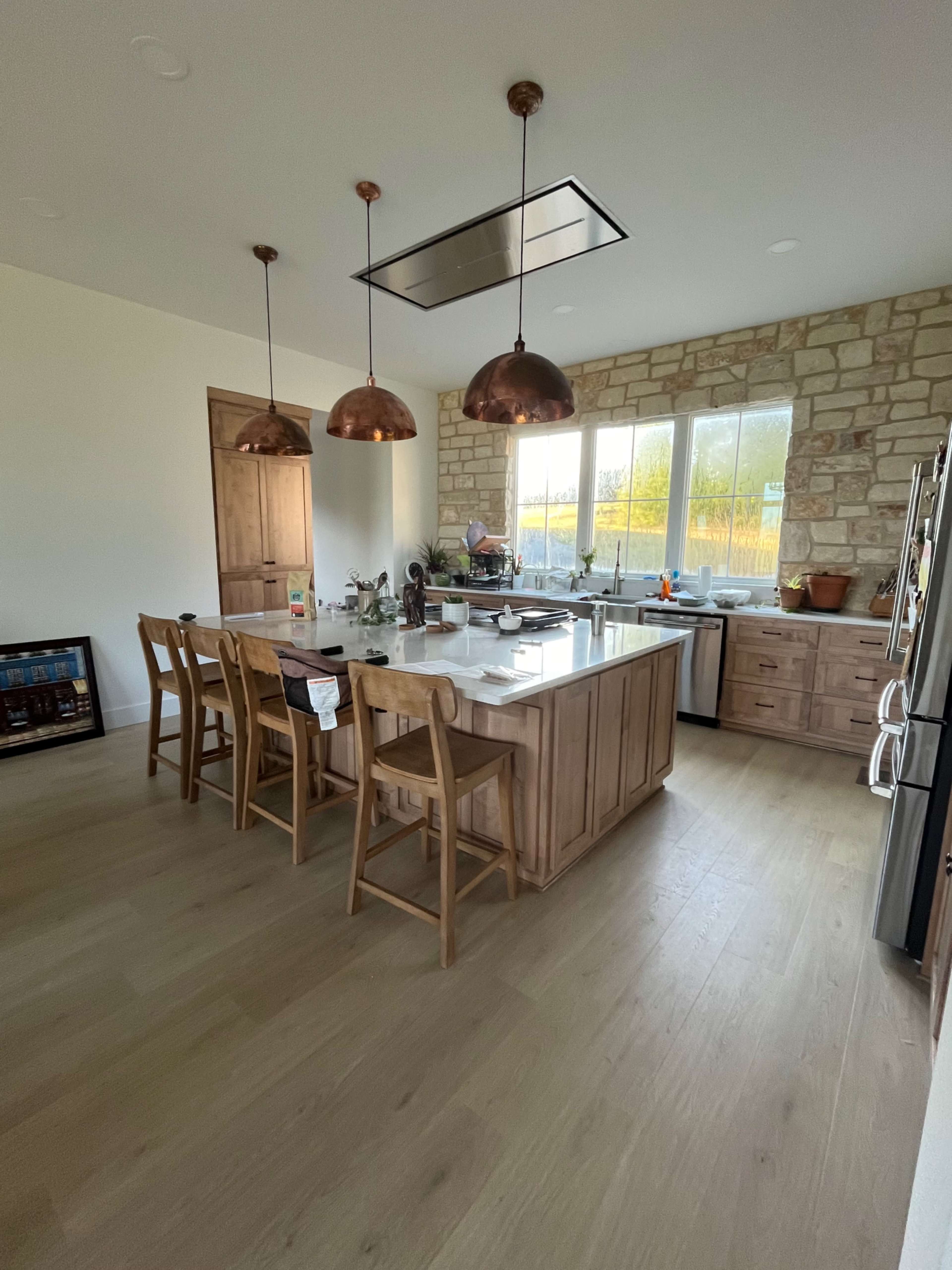 A spacious kitchen features wooden cabinetry, a central island with bar stools, and large windows allowing natural light to illuminate the space.