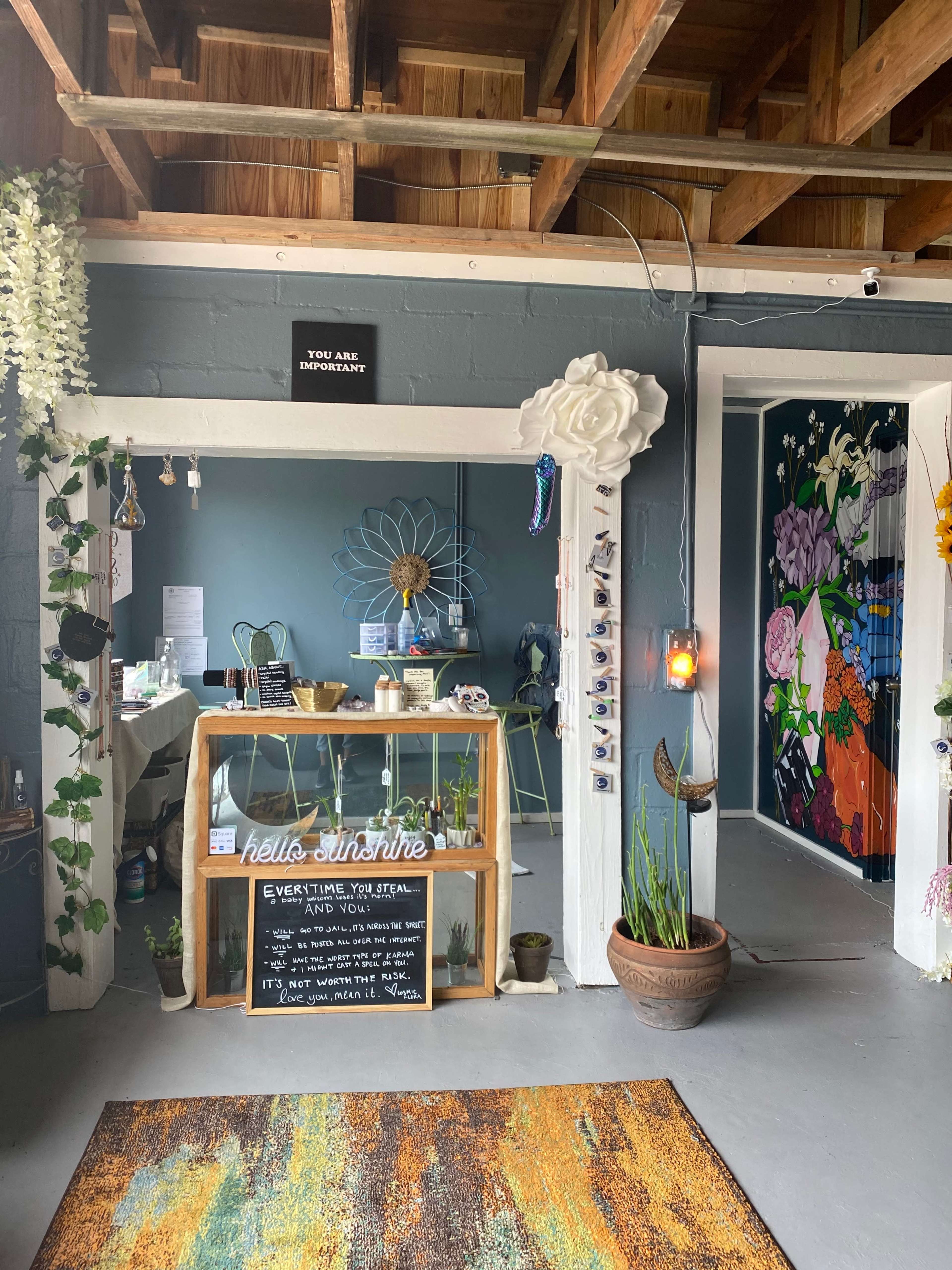 A welcoming interior space with a wooden table displaying a sign that says "hello sunshine" and an open area decorated with plants and colorful artwork on the walls.
