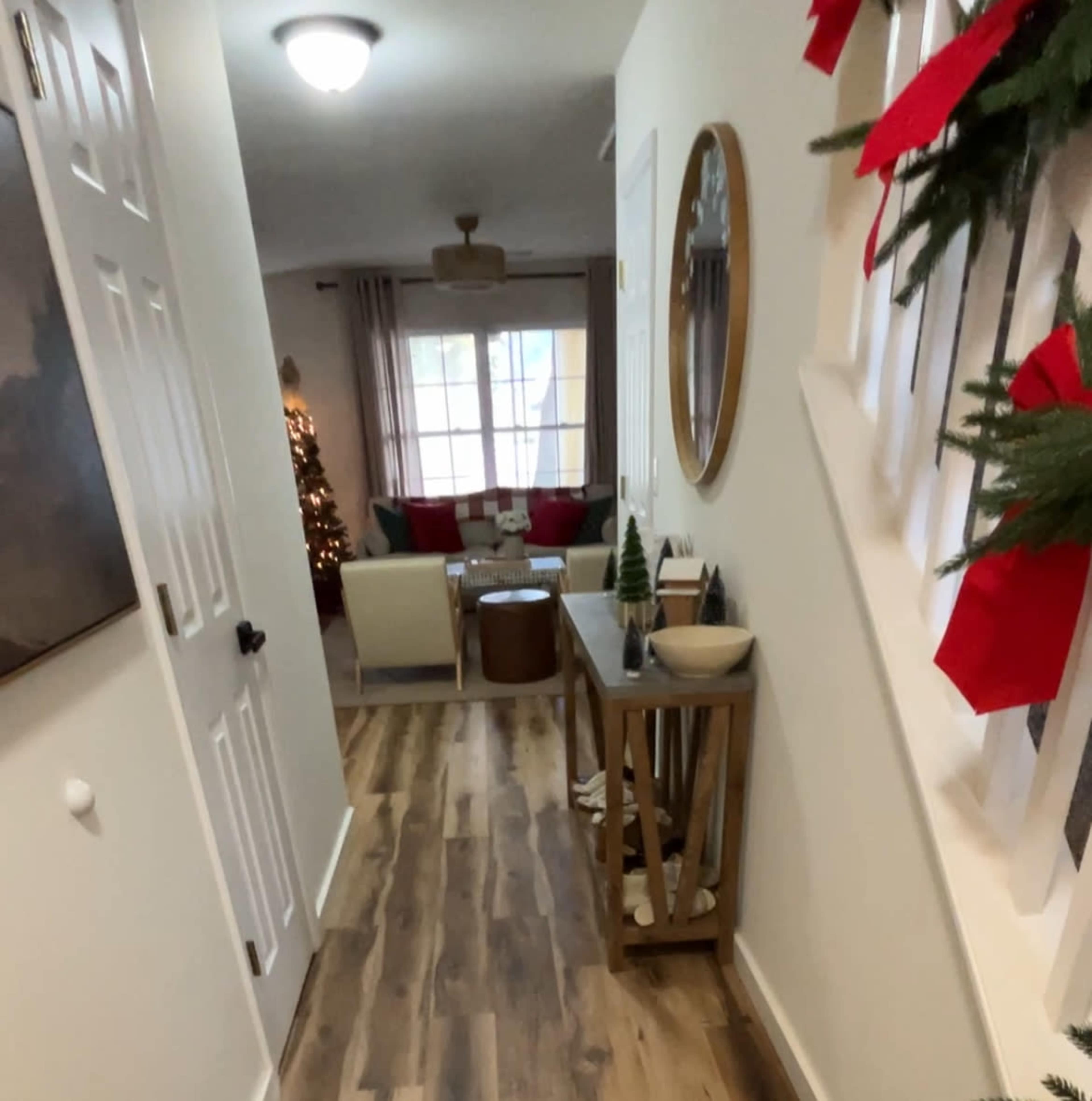 The image shows a hallway leading to a living area, decorated for the holidays, with a visible Christmas tree in the background.
