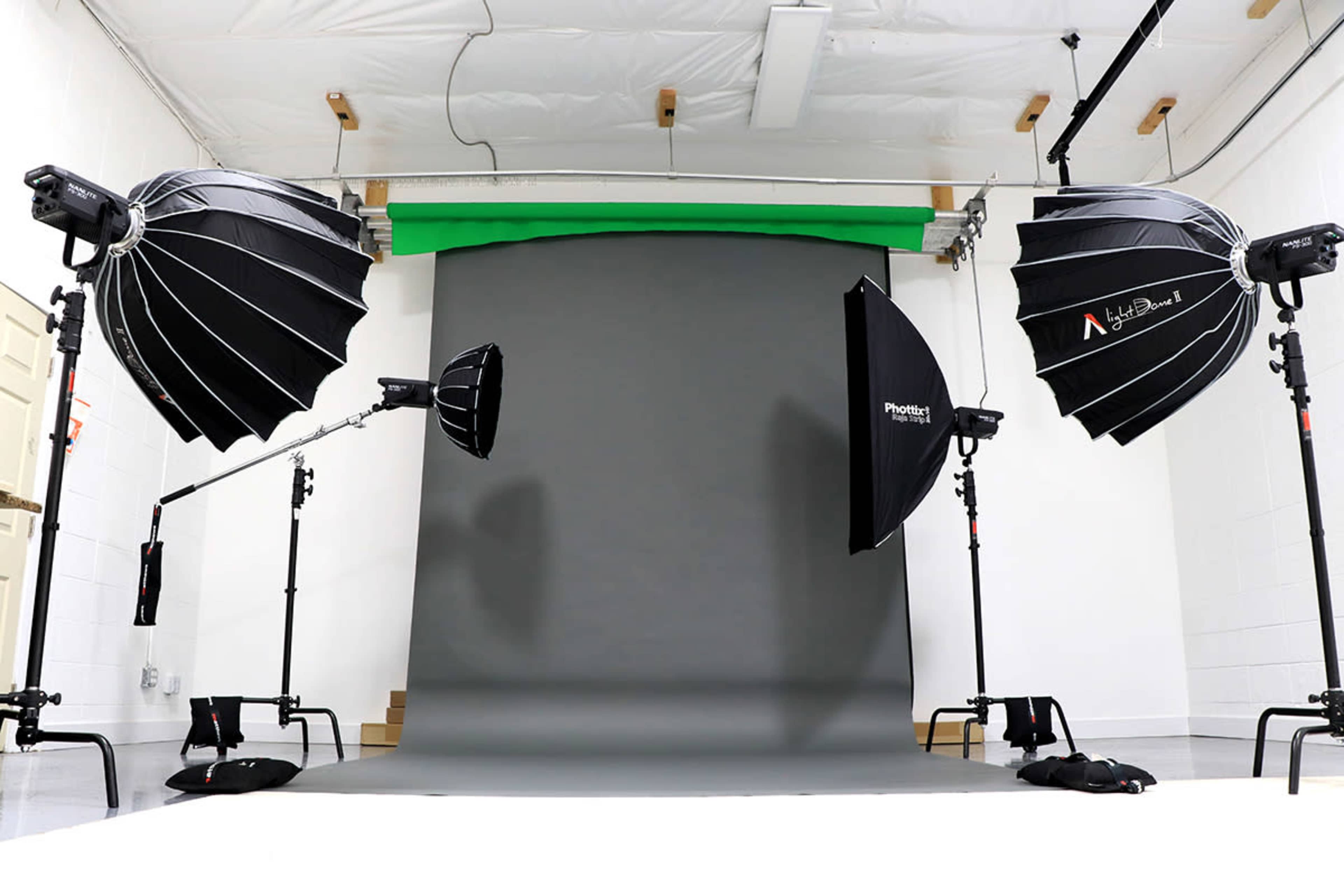 A photography studio setup with multiple light sources and a gray backdrop, complemented by a green screen at the back.