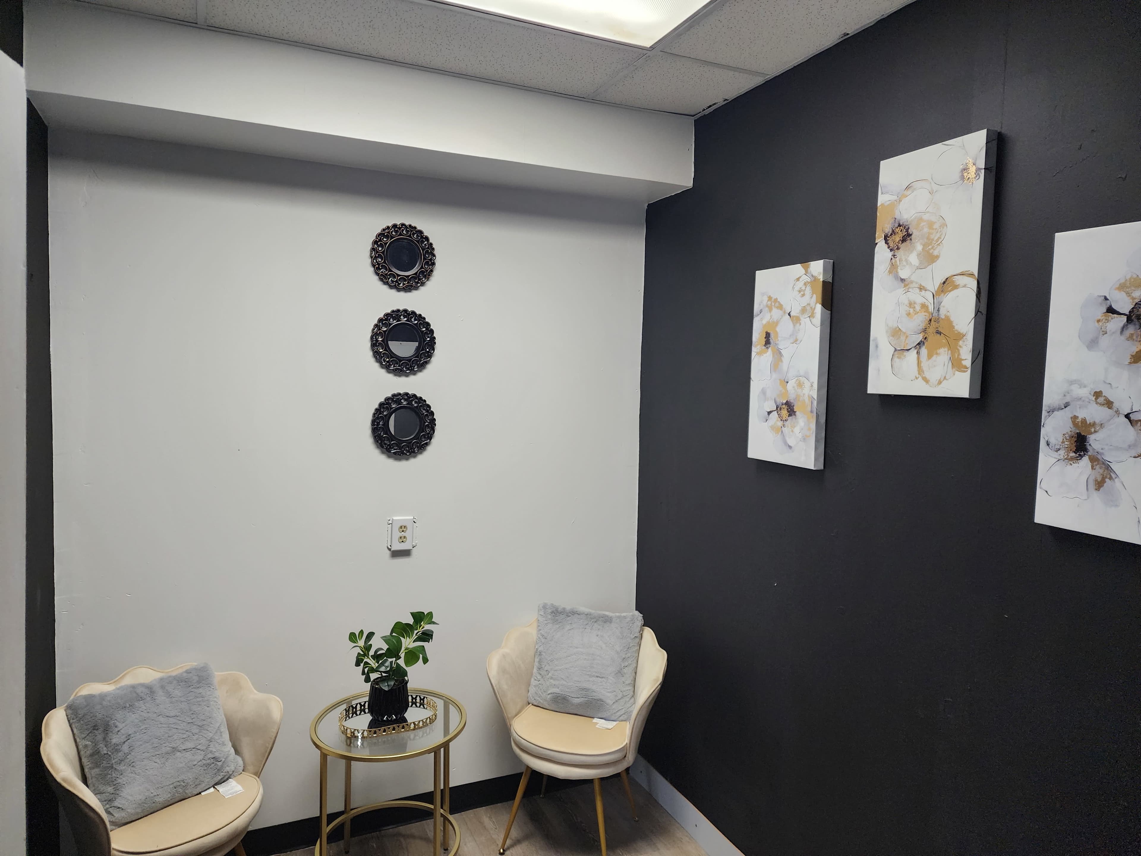 The image shows a small, modern room with two chairs and a round table, featuring decorative wall art and three circular mirrors on one wall.