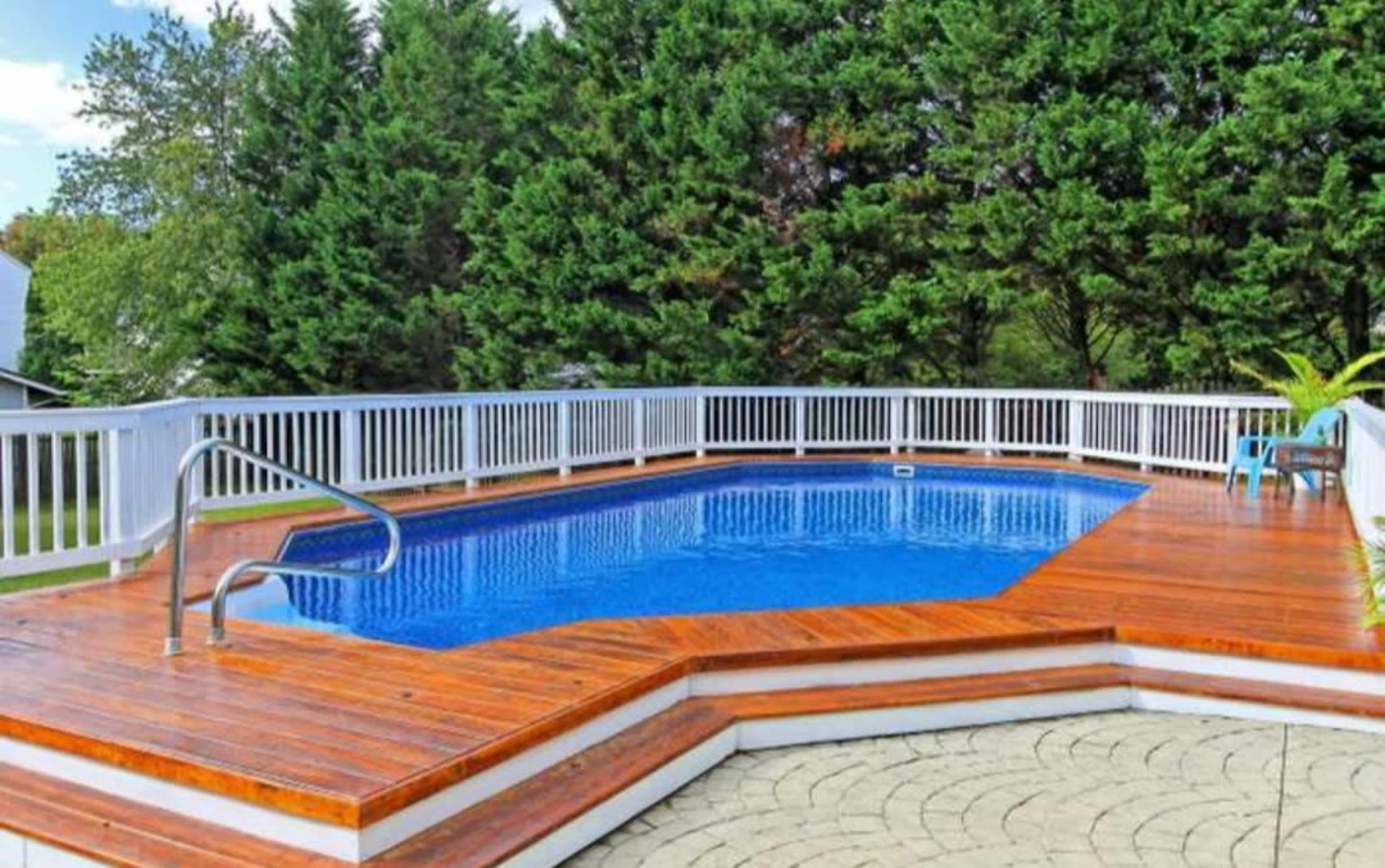 The scene features a wooden deck surrounding a blue swimming pool, bordered by a white railing and lush greenery in the background.