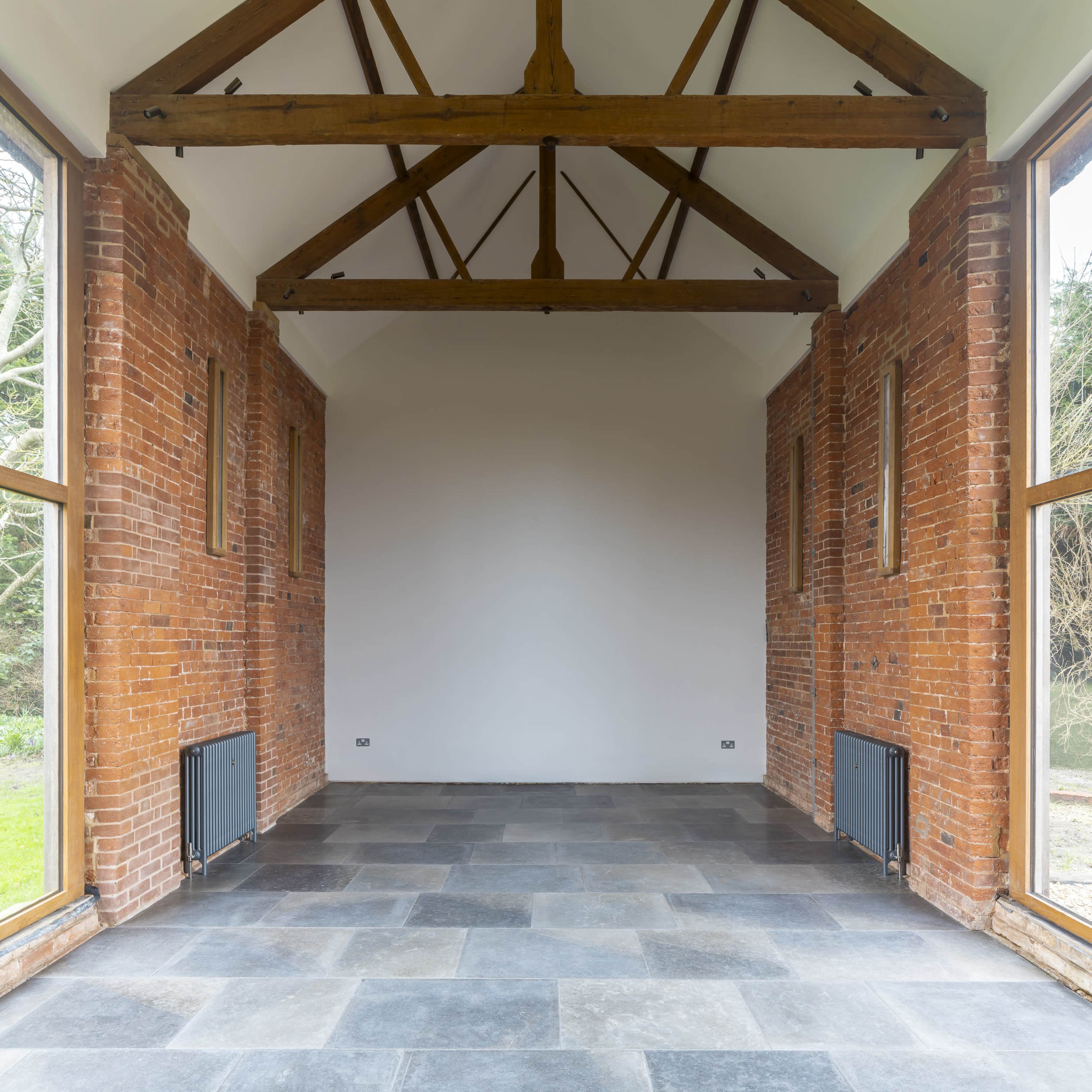 The image shows a spacious interior with exposed brick walls, large windows, and a high wooden beam ceiling.