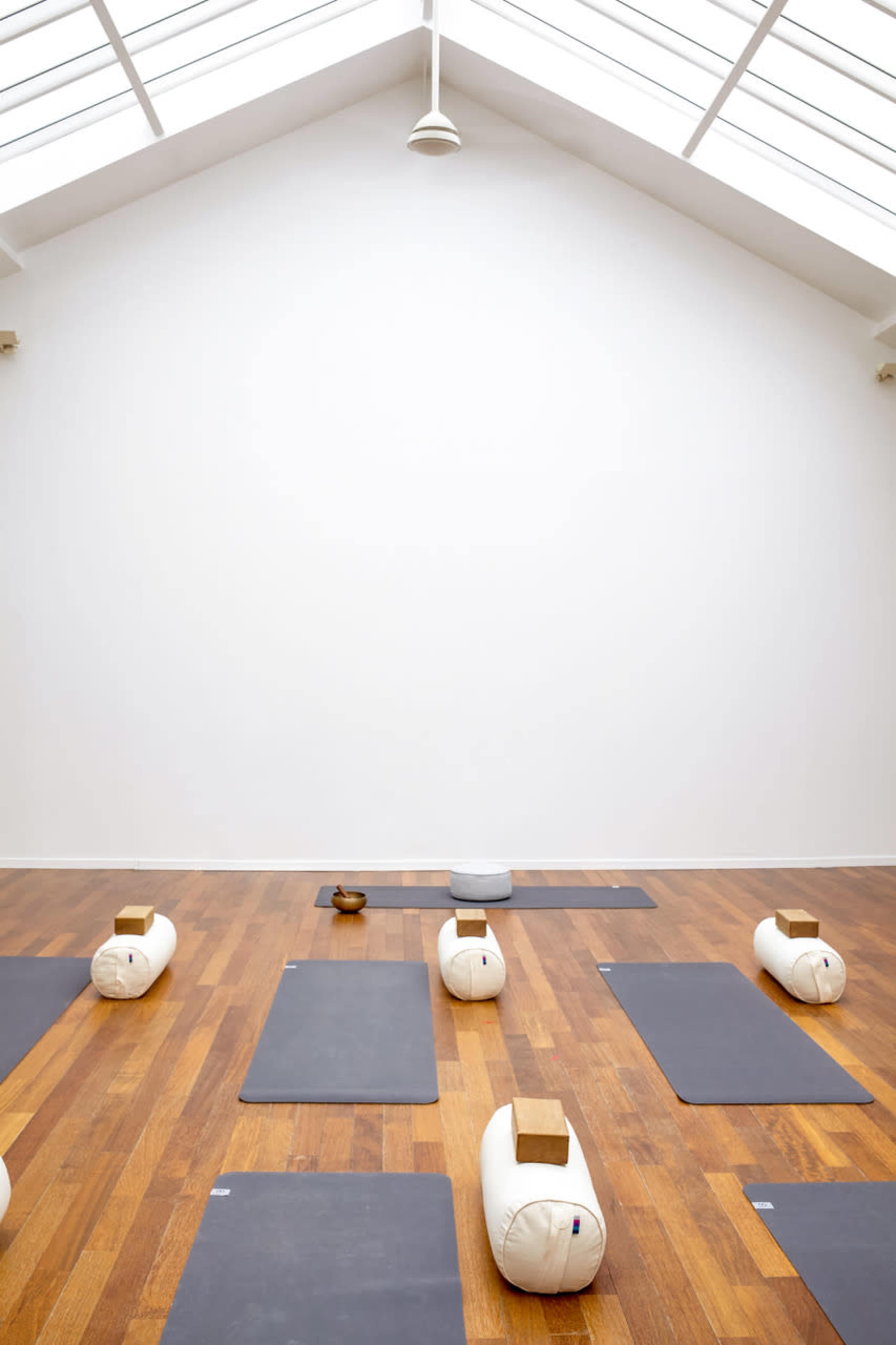 A yoga studio with several mats and bolsters arranged neatly on a wooden floor under a skylight.