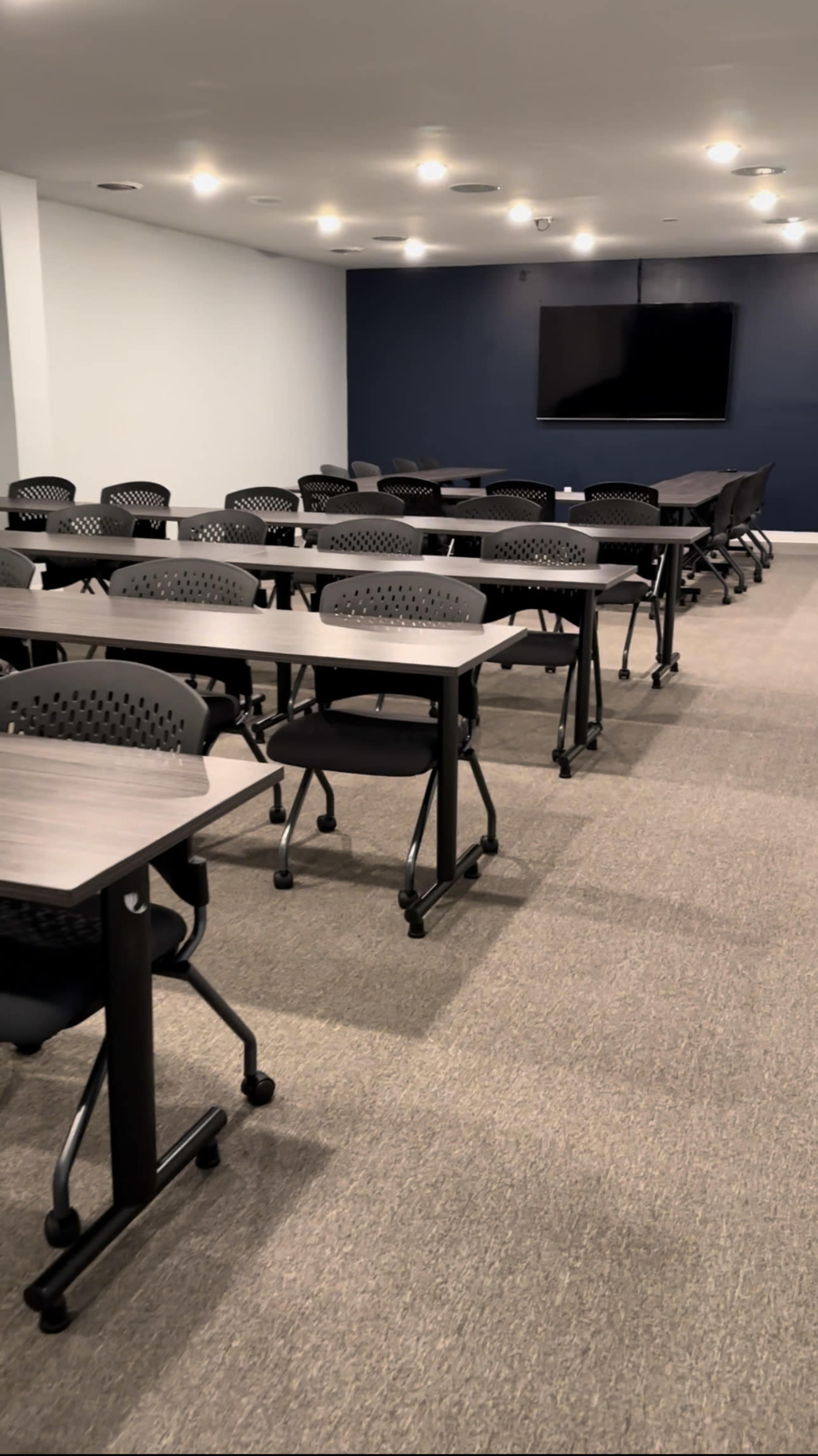 A training room features multiple rows of tables and chairs facing a wall-mounted television.
