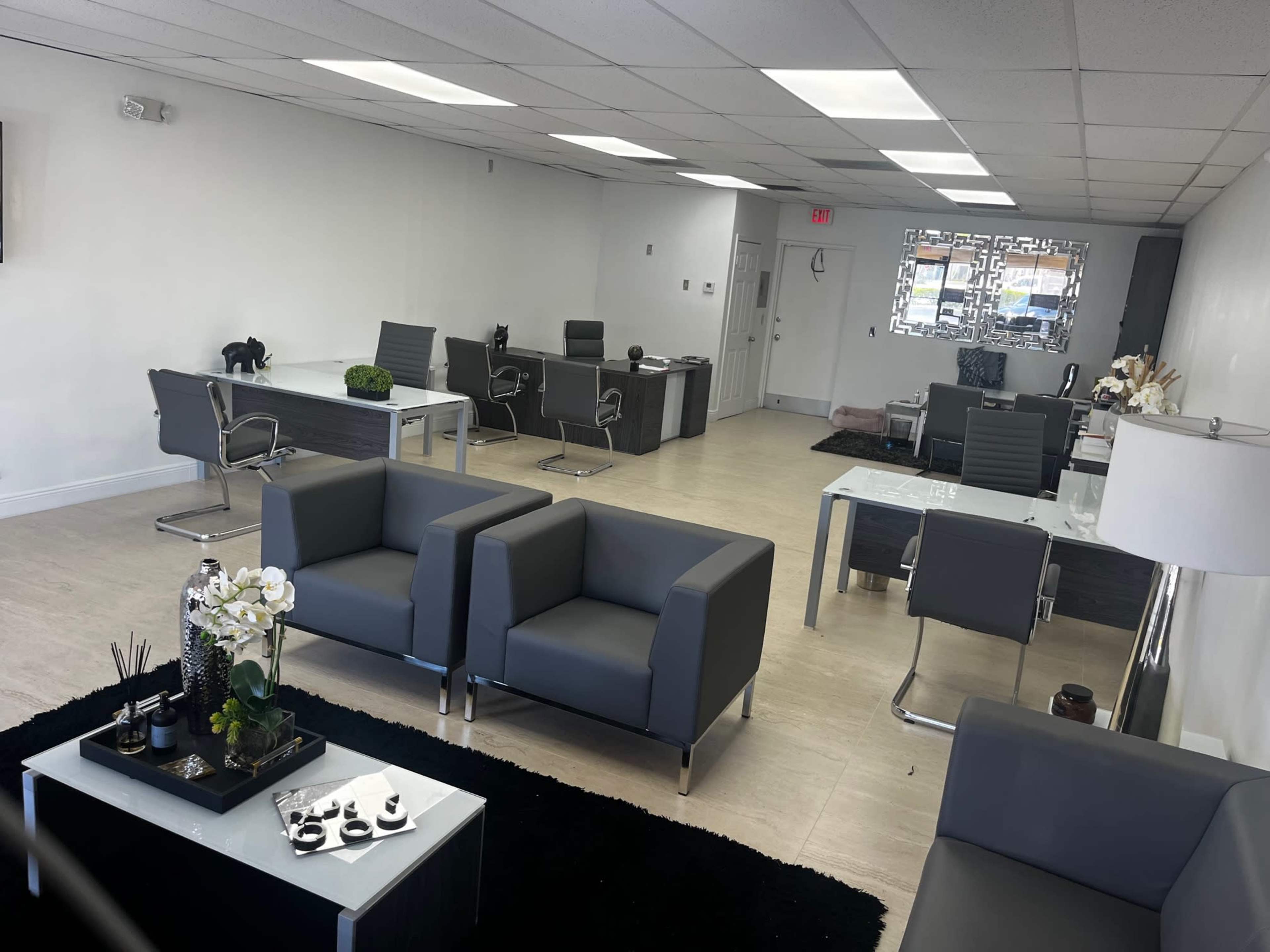 A modern office space with several gray chairs, glass desks, and minimalistic decor.
