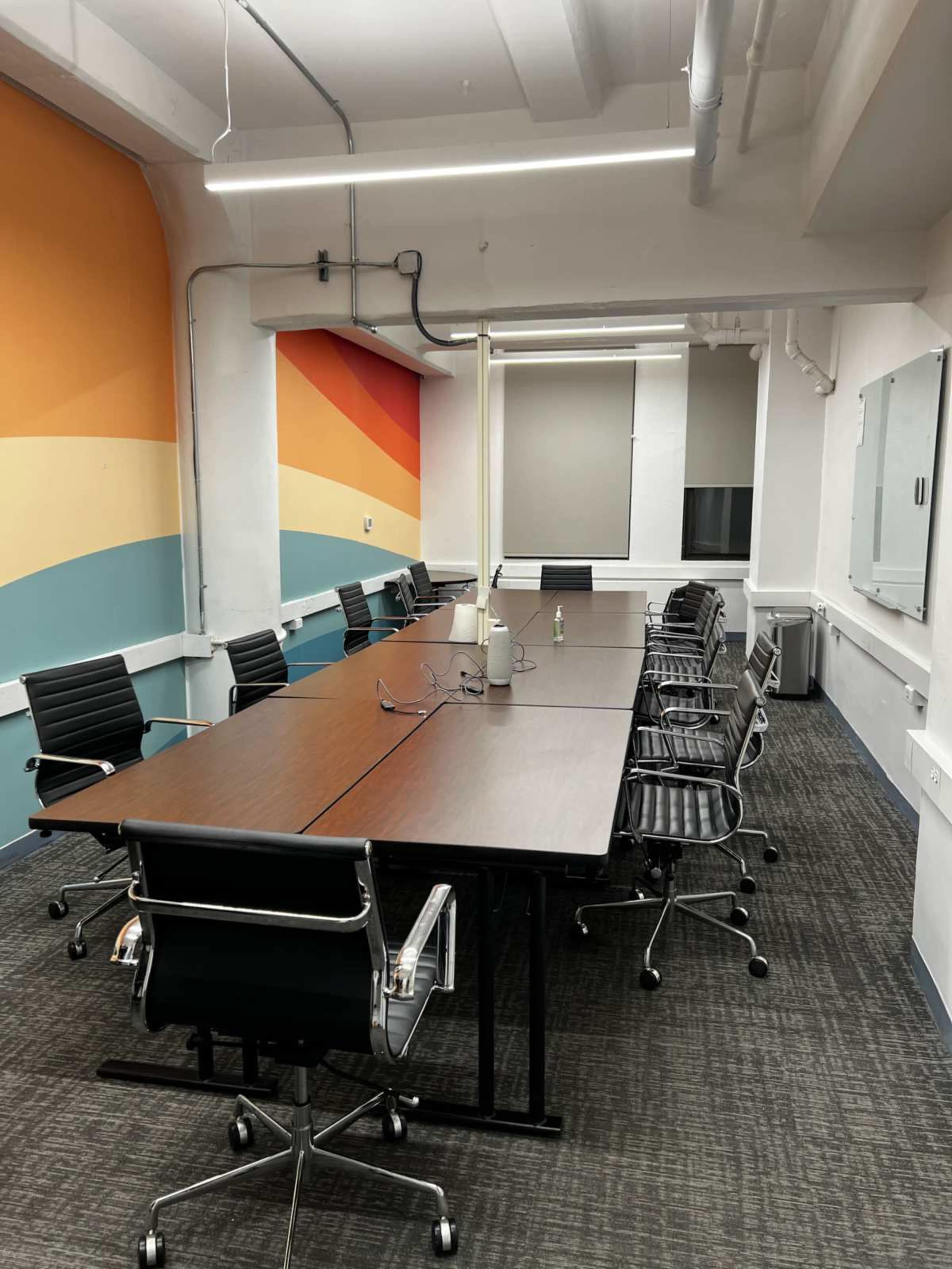 The image shows a modern conference room with a long table, ergonomic chairs, and colorful wall decor.
