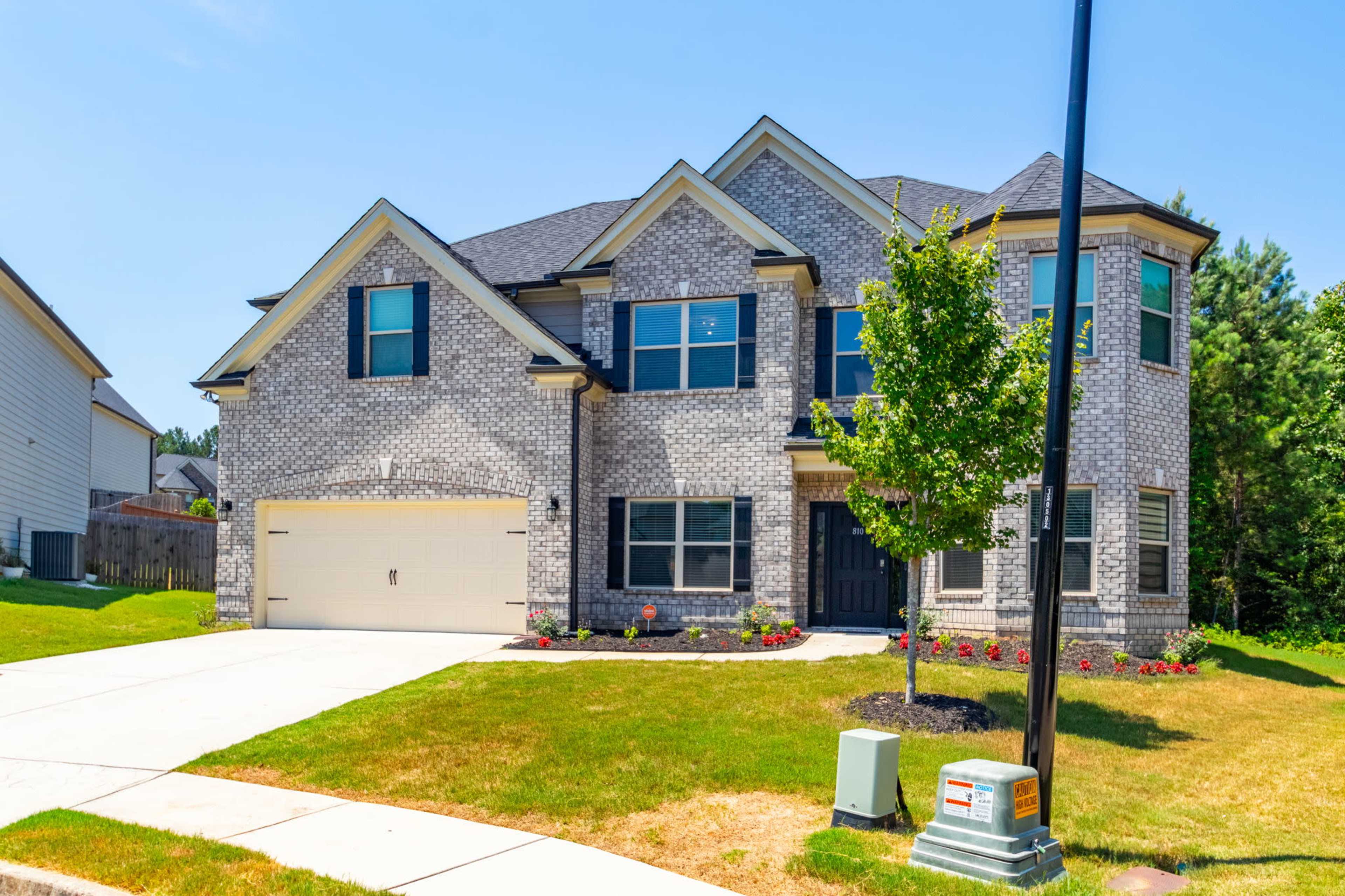 A two-story brick house with a landscaped yard and a driveway leads to a double garage.