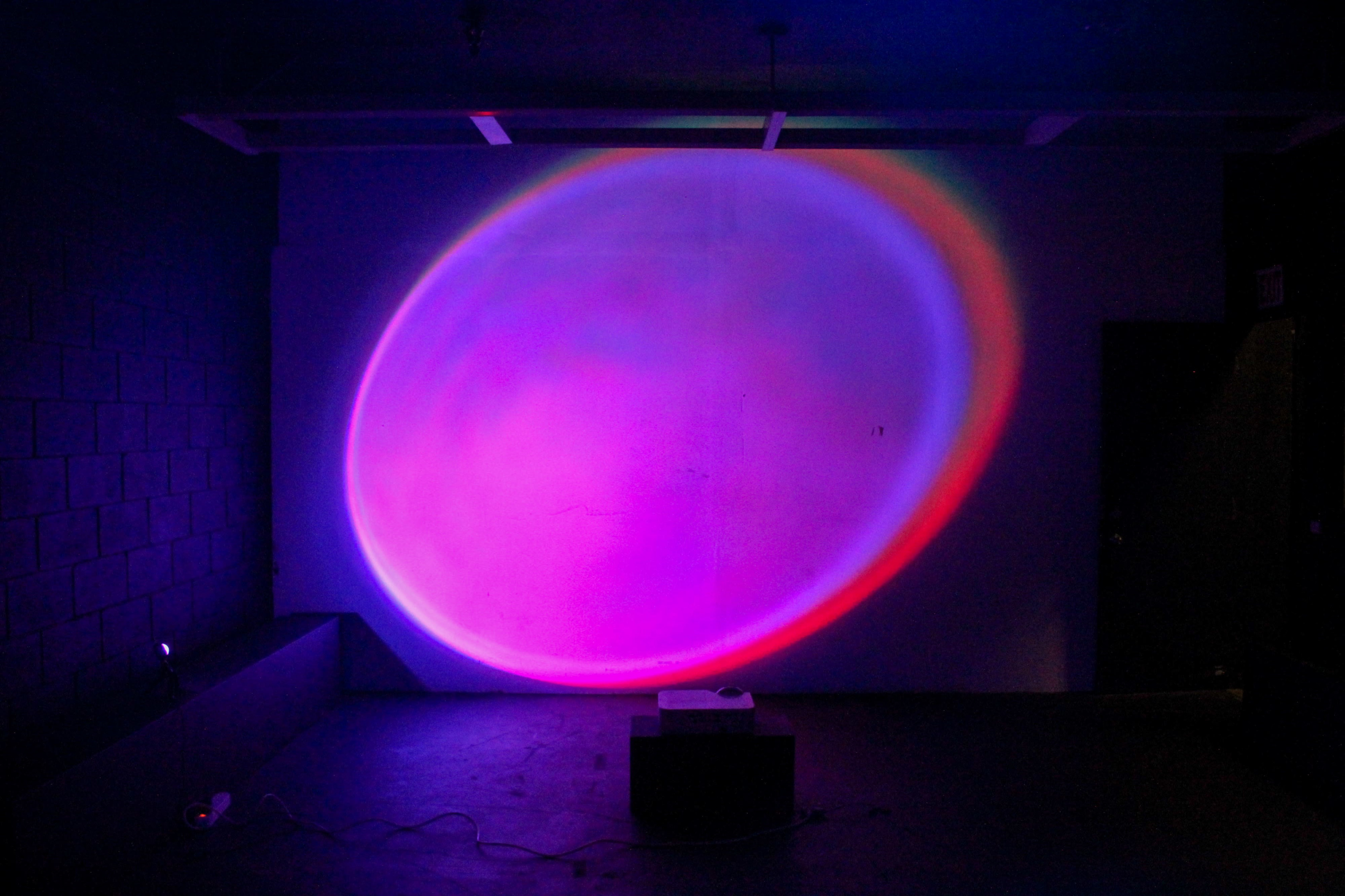 A colorful light projection illuminates a wall in a dimly lit room.
