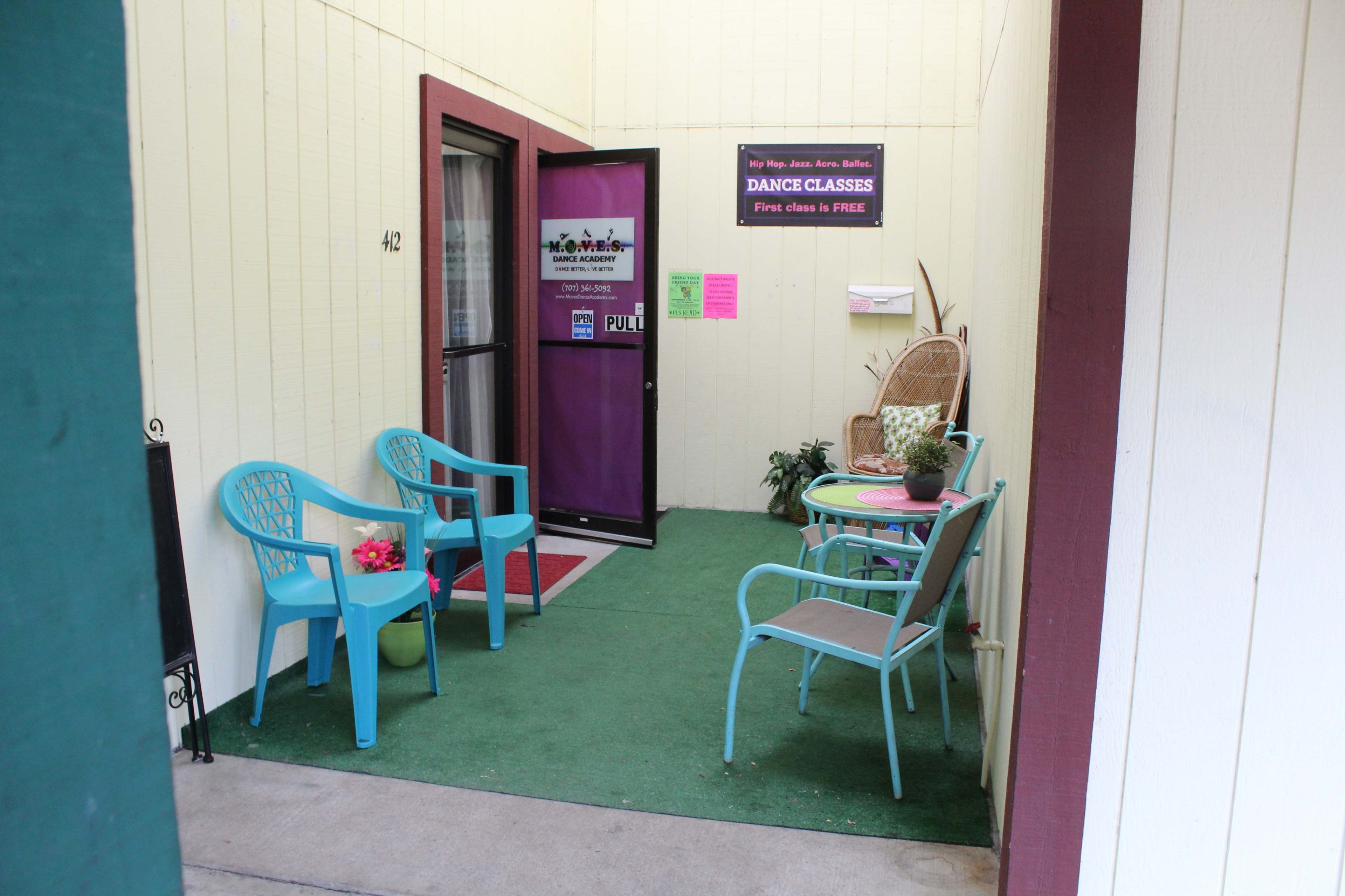 A small entrance area with chairs and a table adorned with plants and a sign for dance classes.