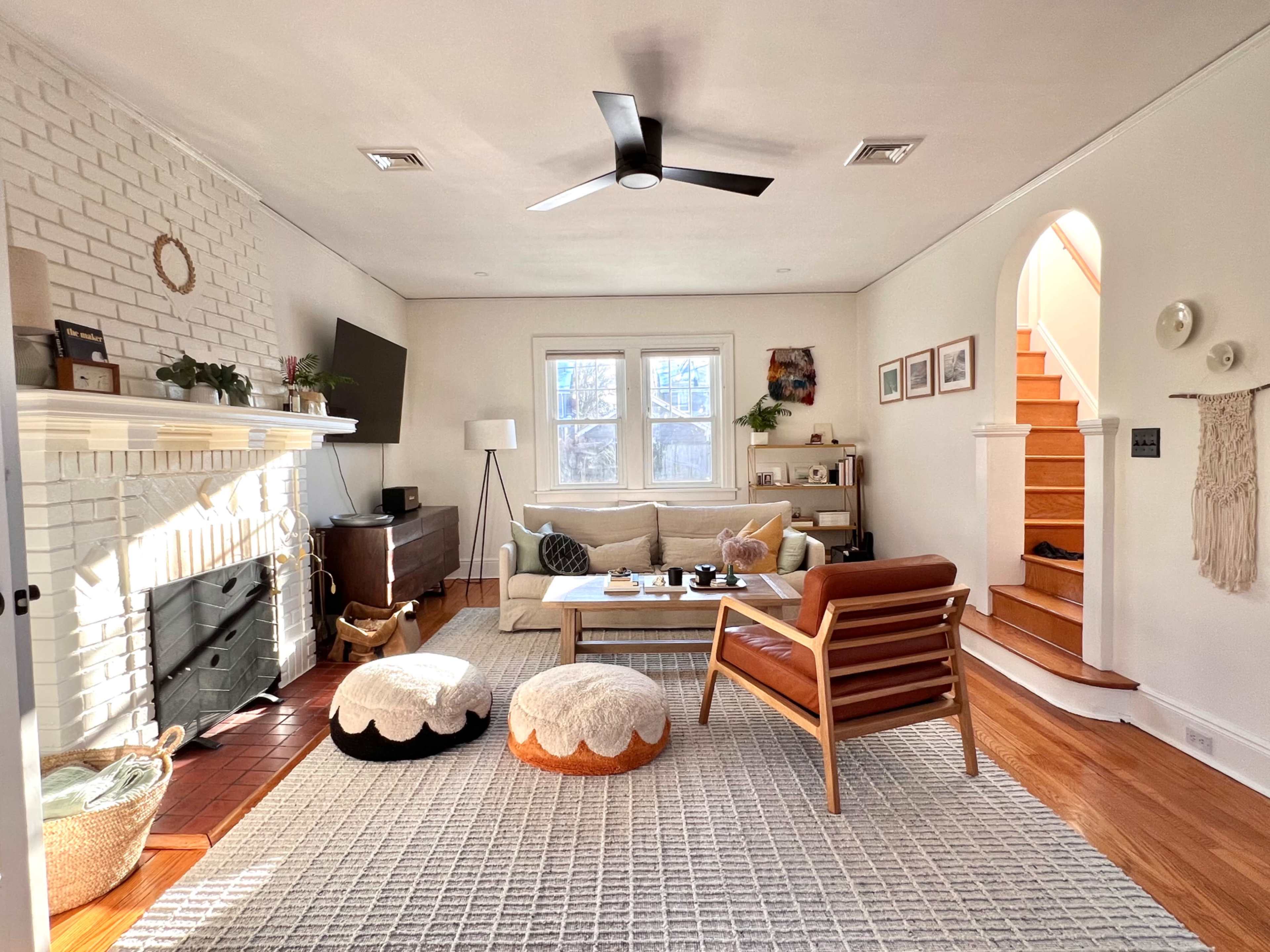 The living room features a white brick fireplace, a comfortable sofa, a wooden coffee table, and a staircase leading to an upper level.