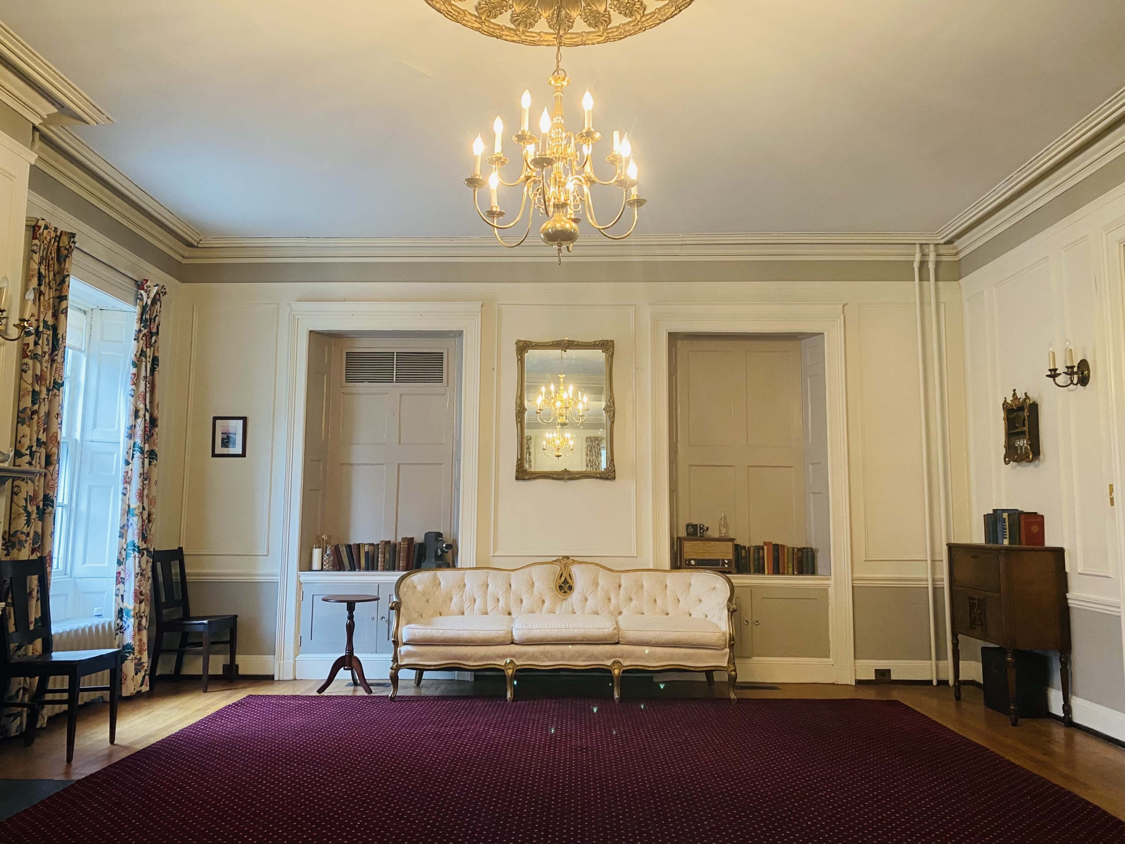 A spacious room featuring a chandelier, a mirror above a sofa, and bookshelves flanking the walls.
