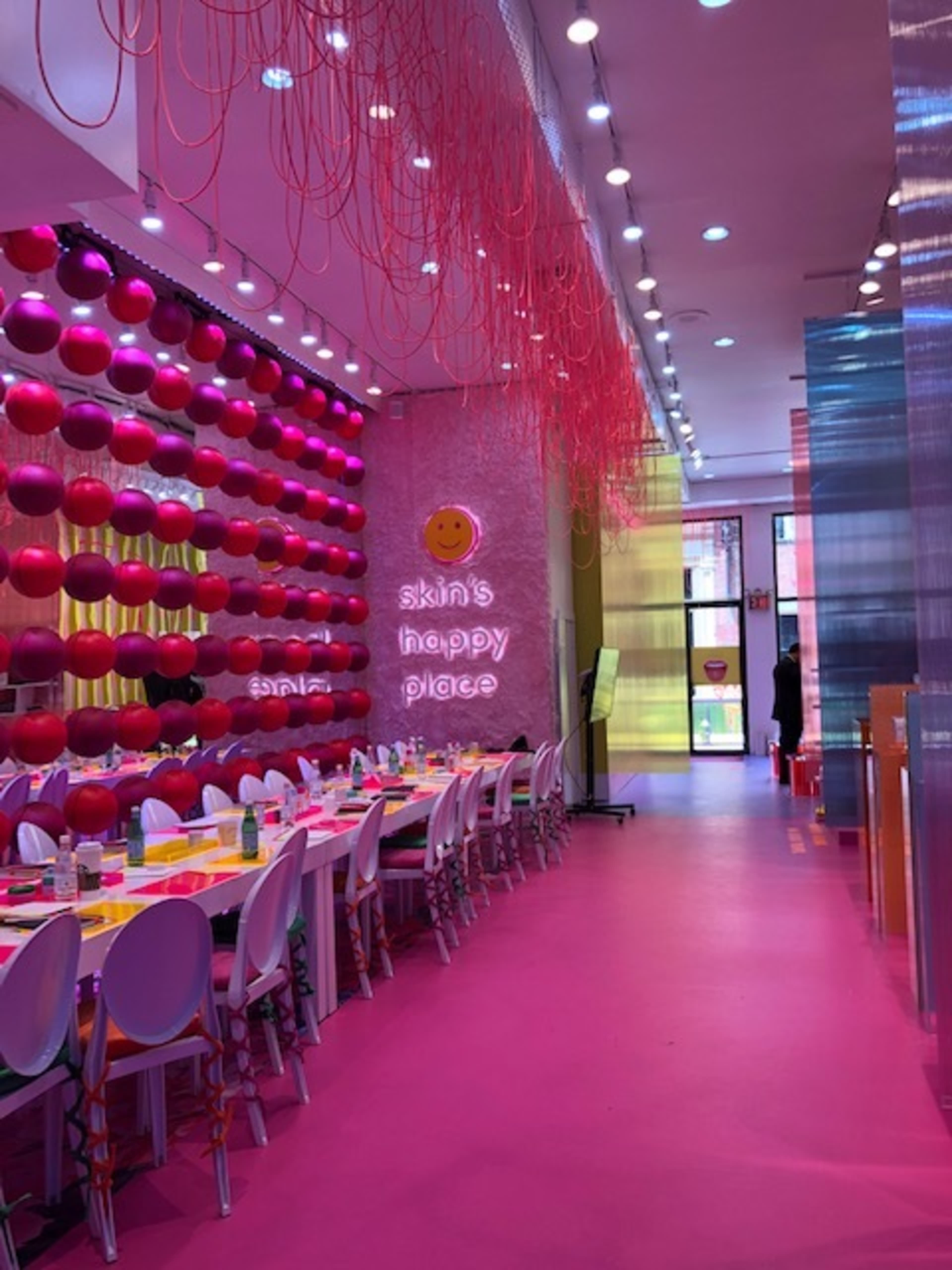 A colorful restaurant interior with pink walls, round pink and red decorations, and a long table set for dining.