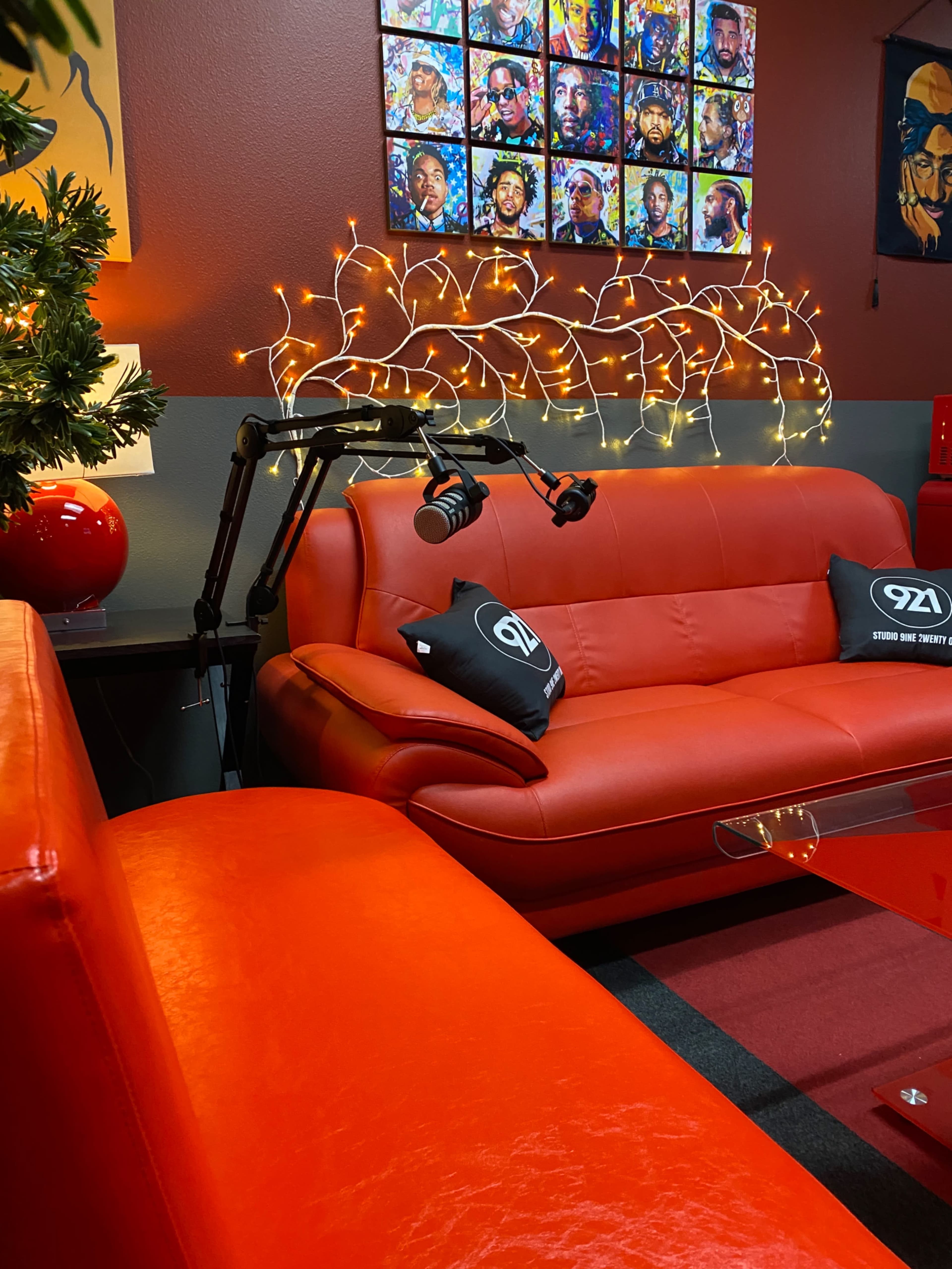 The image shows a modern lounge area with orange leather sofas, a glass coffee table, and decorative fairy lights above a collection of portraits on the wall.